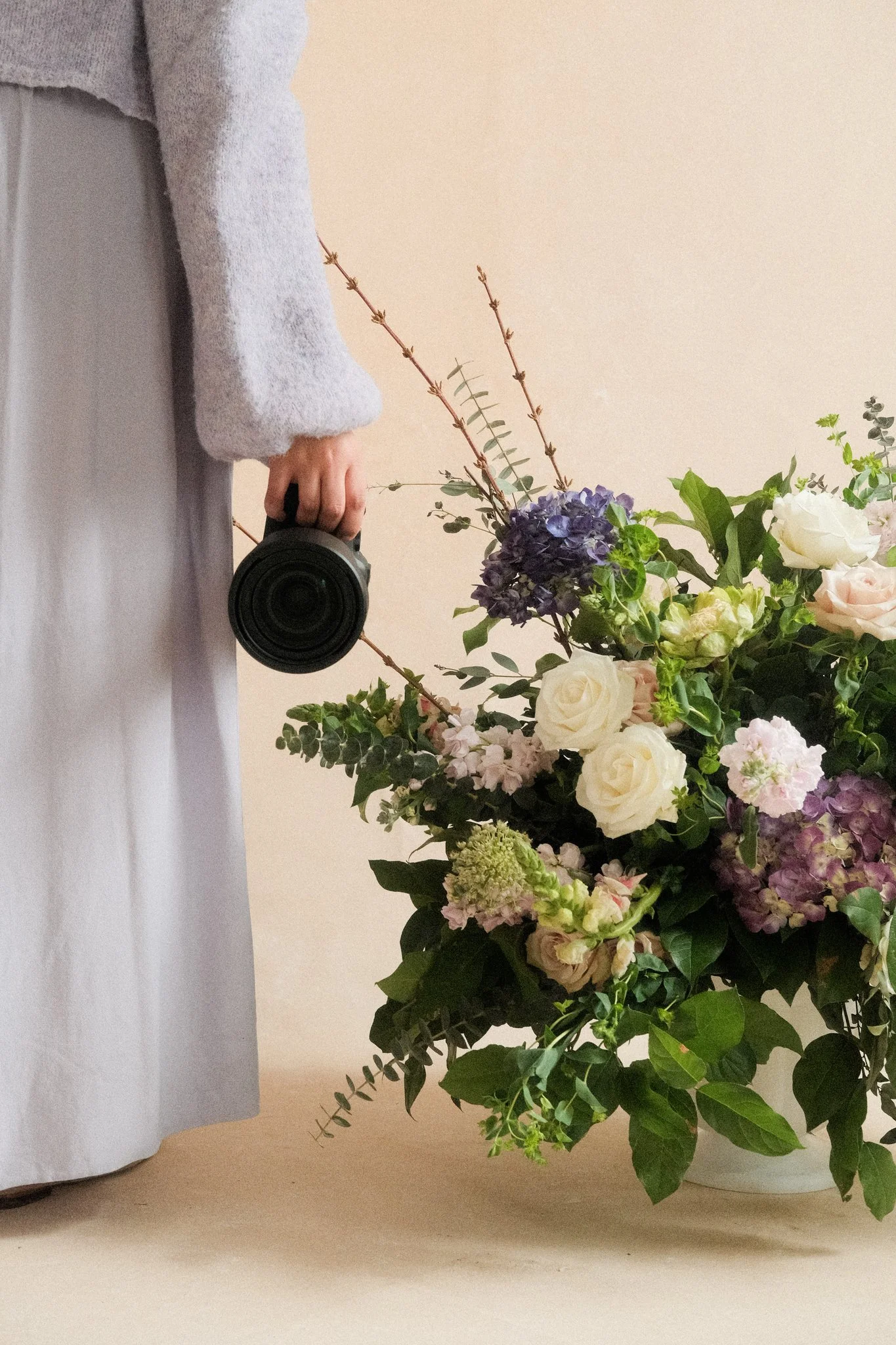 photographer holding camera lens beside large floral arrangement against Chasing Stone Sandstone canvas backdrop