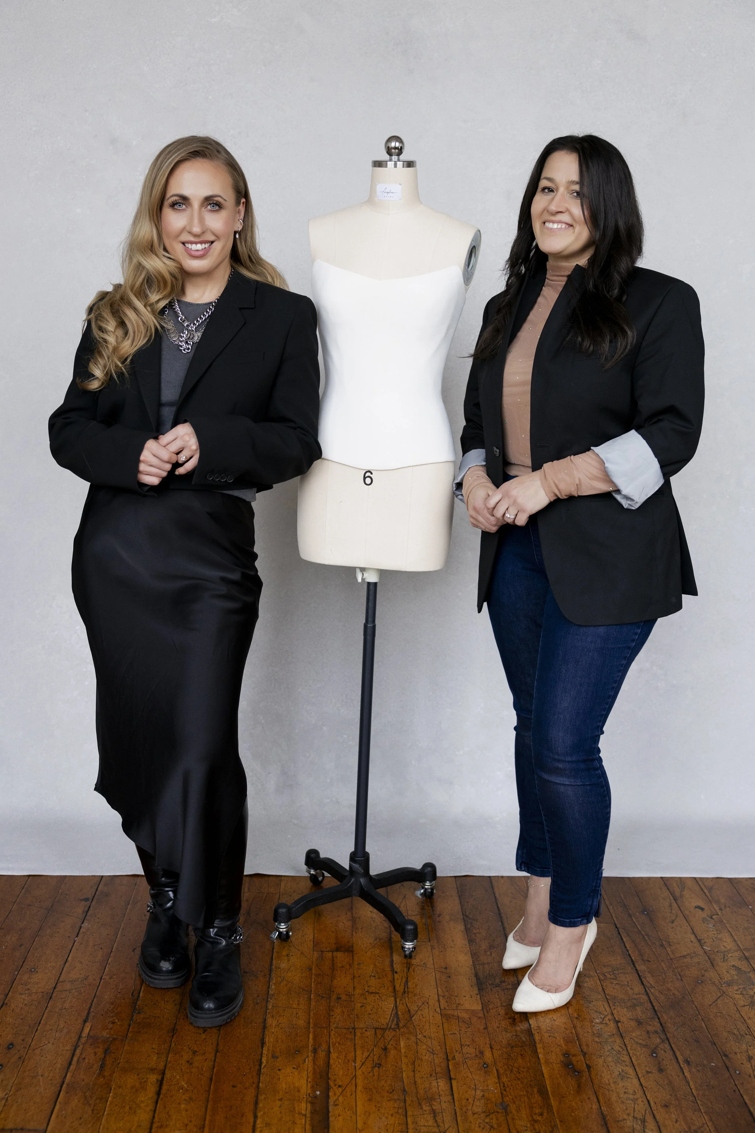 two fashion photographers standing with a dress form mannequin in a photography studio with hardwood floors and grey backdrop