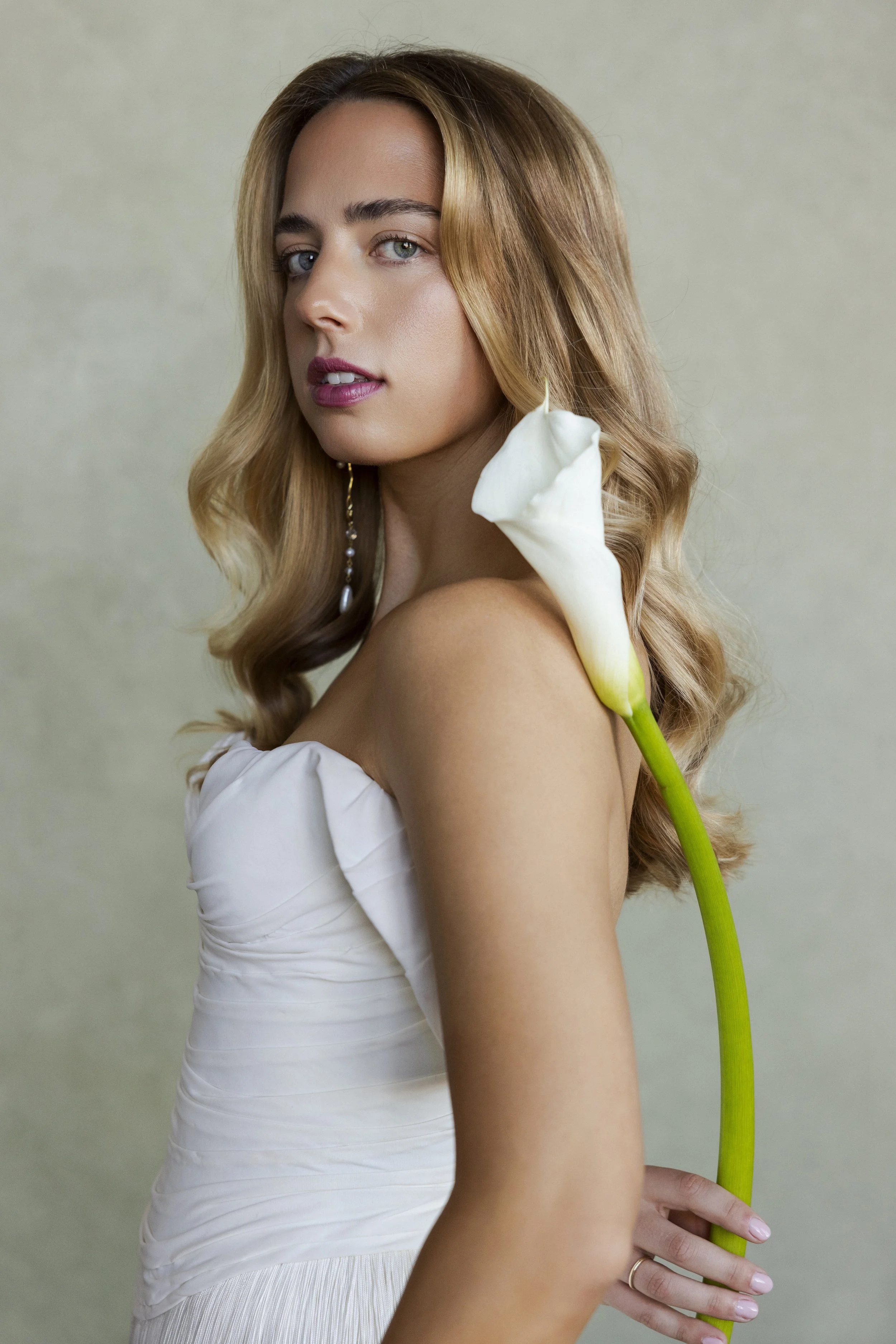 bridal portrait of woman holding a white calla lily against a soft green textured backdrop"