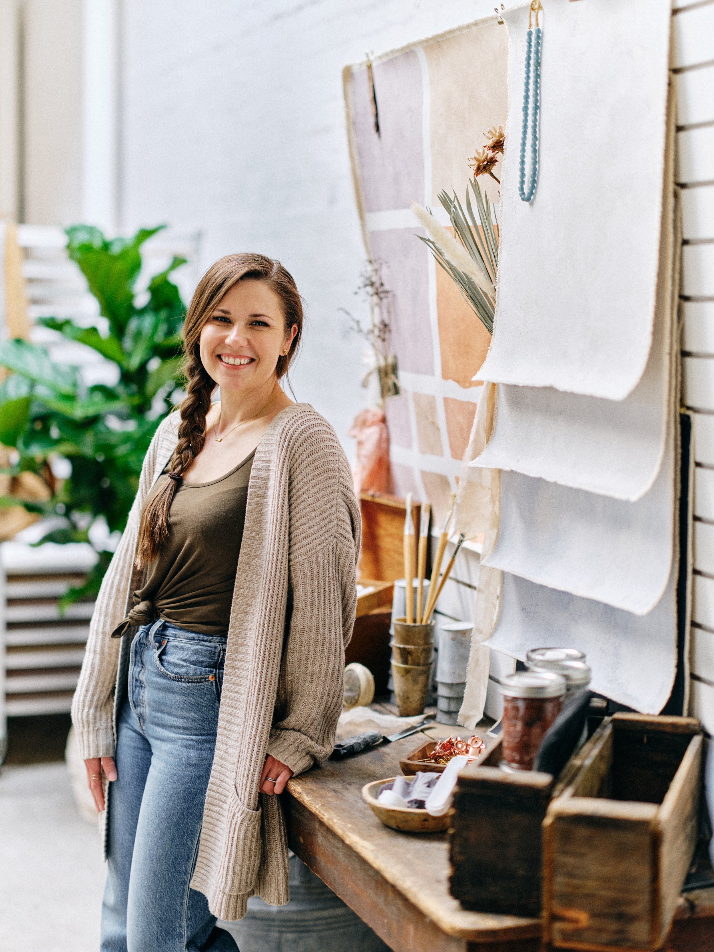 Chasing Stone artist in studio workspace with hand-painted canvas backdrop samples hanging on display rack and painting supplies
