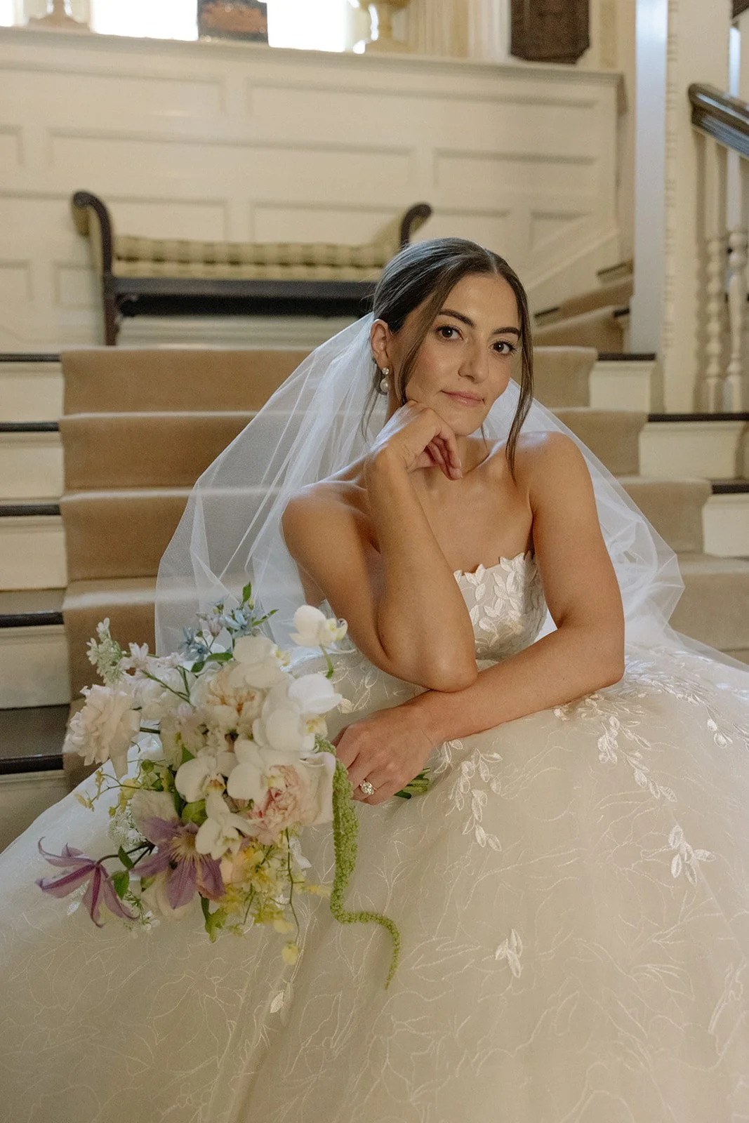 Bride sitting on a staircase holding a bouquet during a wedding portrait inside a venue