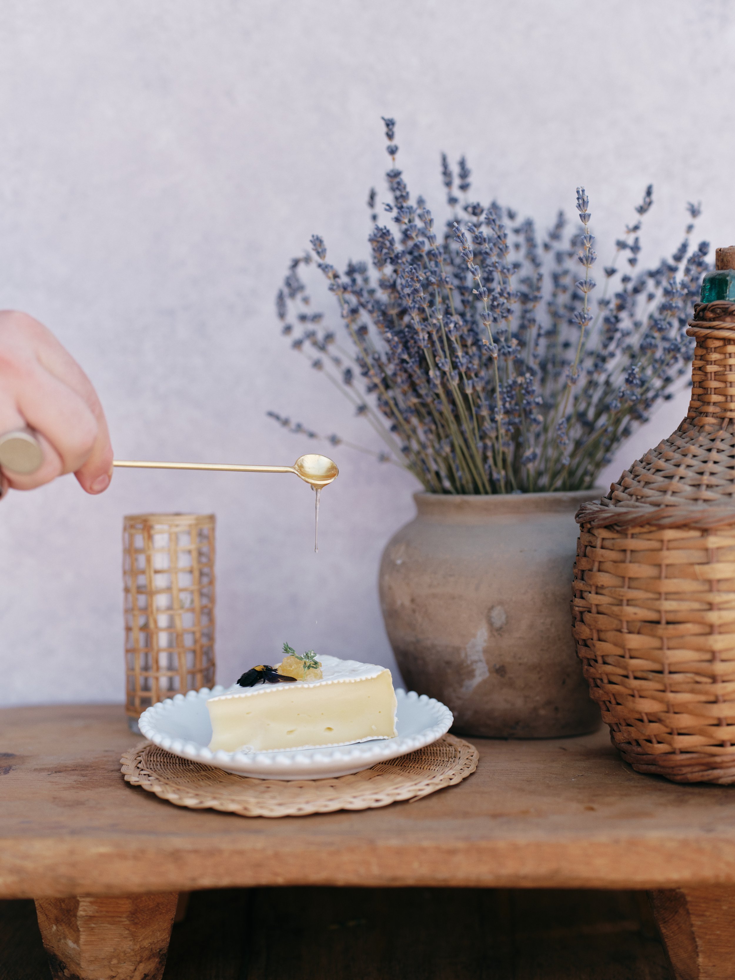 Honey being drizzled over a slice of cake on a rustic wooden table with lavender in the background against a soft neutral textured backdrop