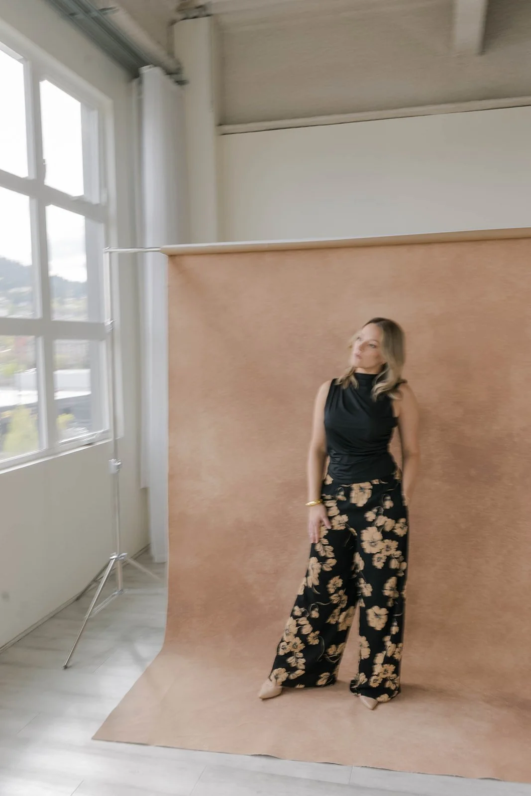 Photographer's studio setup showing a full-length personal branding portrait against a large warm terracotta hand-painted canvas backdrop on a backdrop stand, demonstrating how Chasing Stone backdrops perform in natural light studio environments