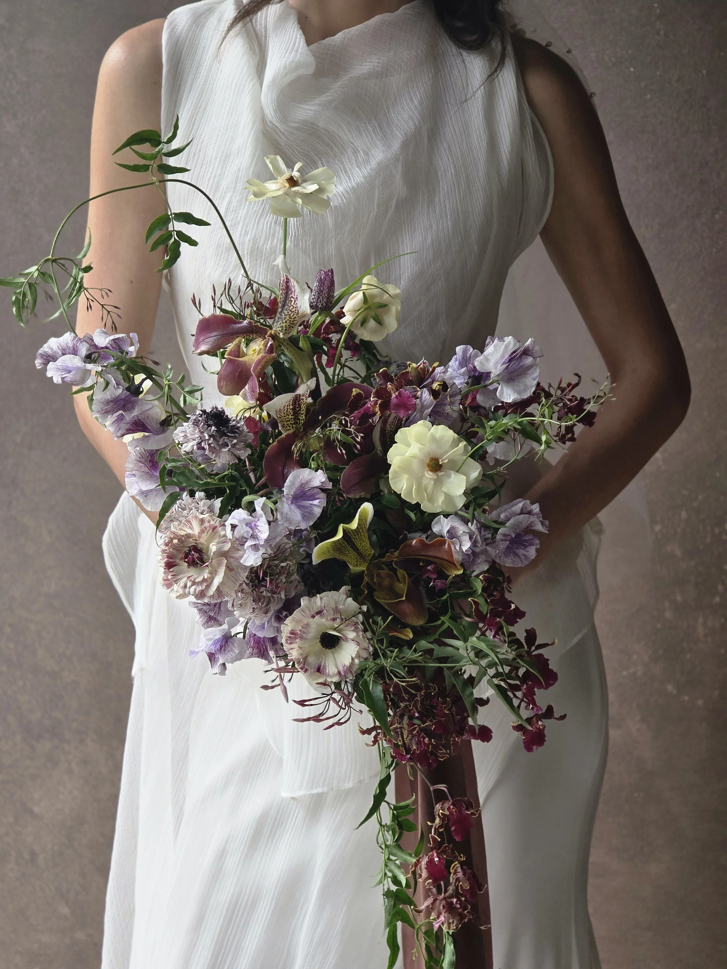 Bride in white textured gown holding cascading purple and burgundy bouquet against a Chasing Stone Graphite hand-painted canvas backdrop