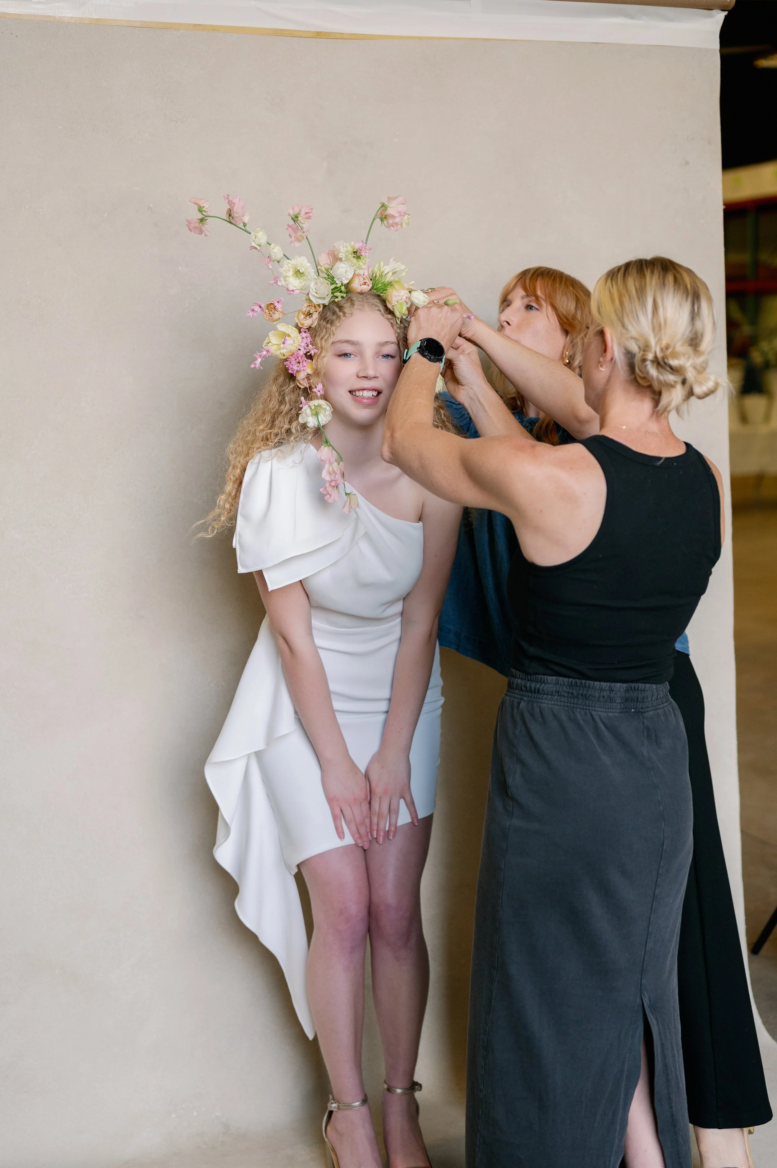 Model being styled with a floral headpiece in front of a photography backdrop during a portrait session
