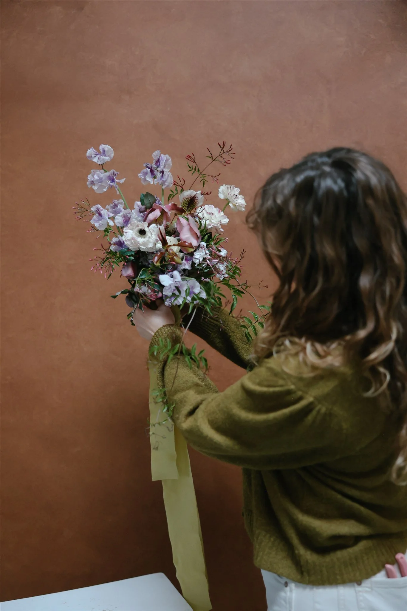 woman holding a bouquet against a terracotta hand-painted canvas backdrop