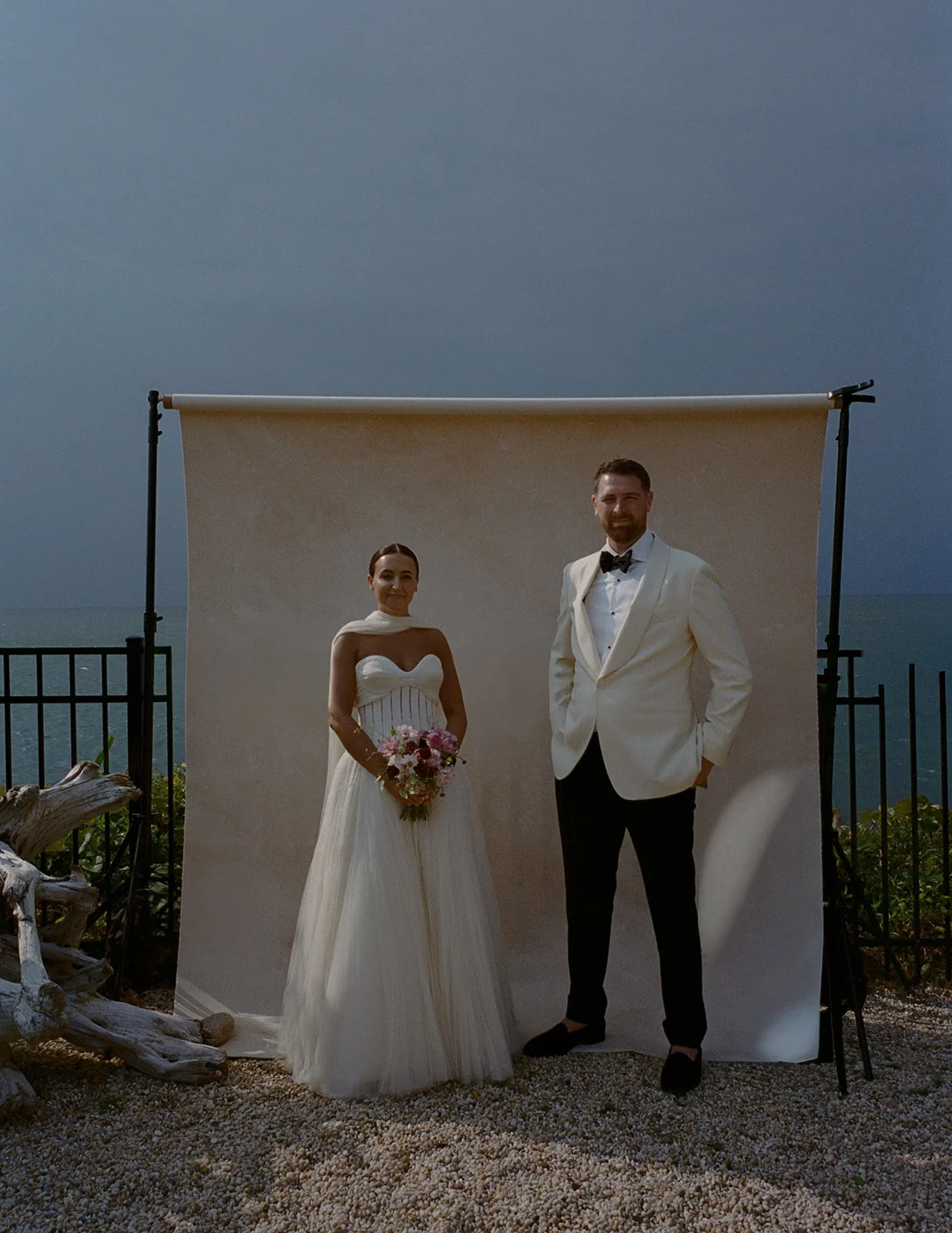 outdoor wedding portrait photographed in front of a canvas backdrop mounted on C-stands near the ocean, demonstrating an outdoor backdrop photography setup