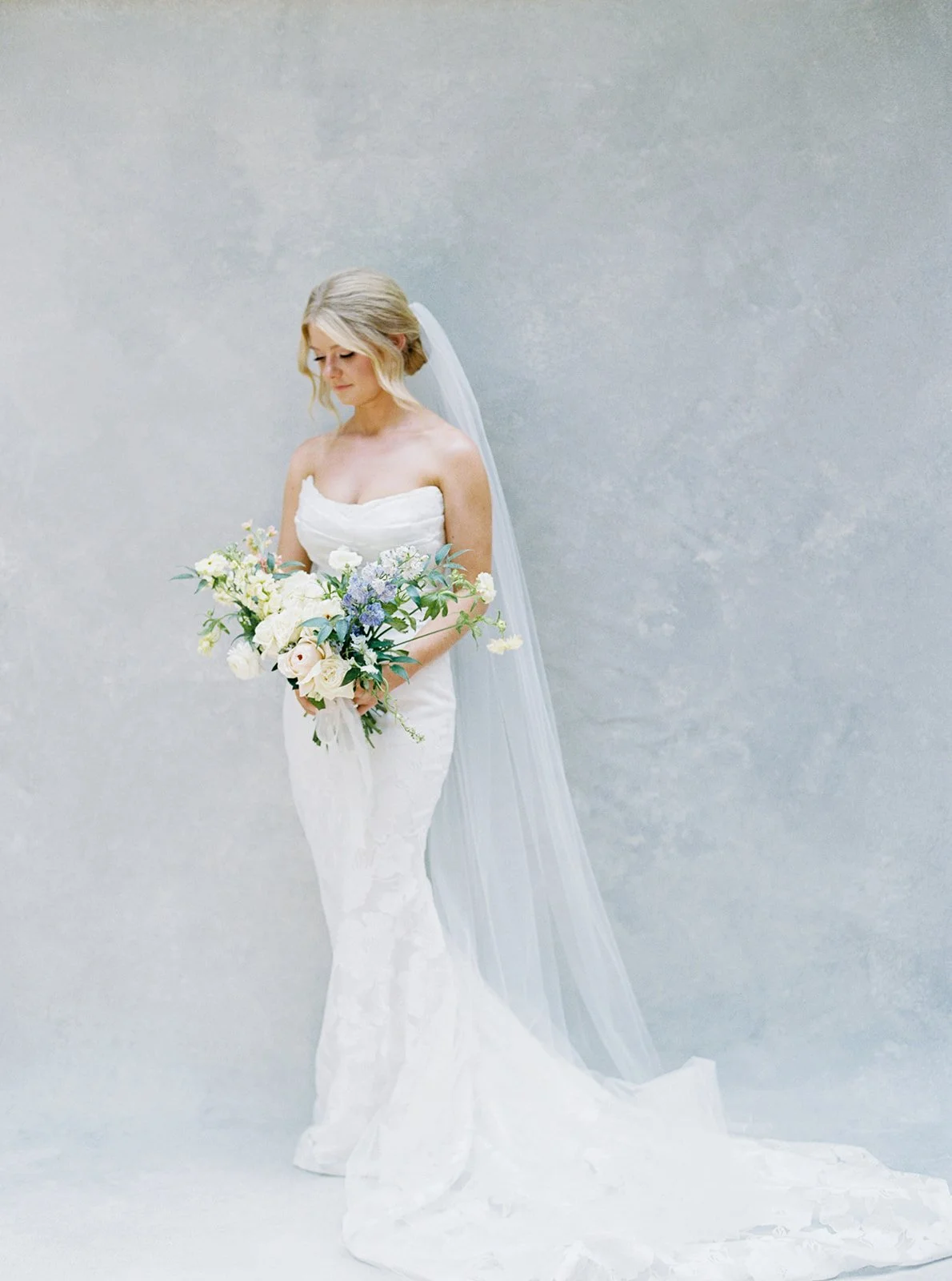 bride in lace mermaid gown with cathedral veil standing in front of gray hand-painted canvas backdrop
