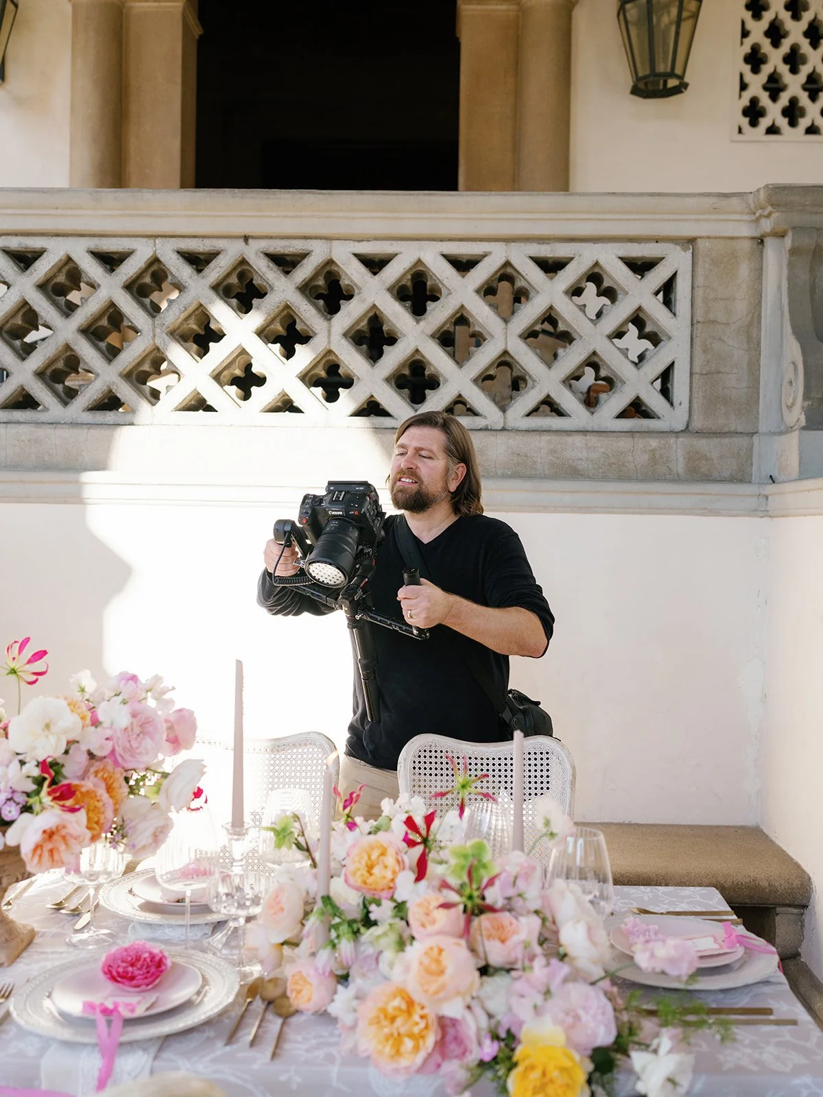 photographer capturing a wedding tablescape with pink and peach garden roses on a Spanish-style outdoor terrace