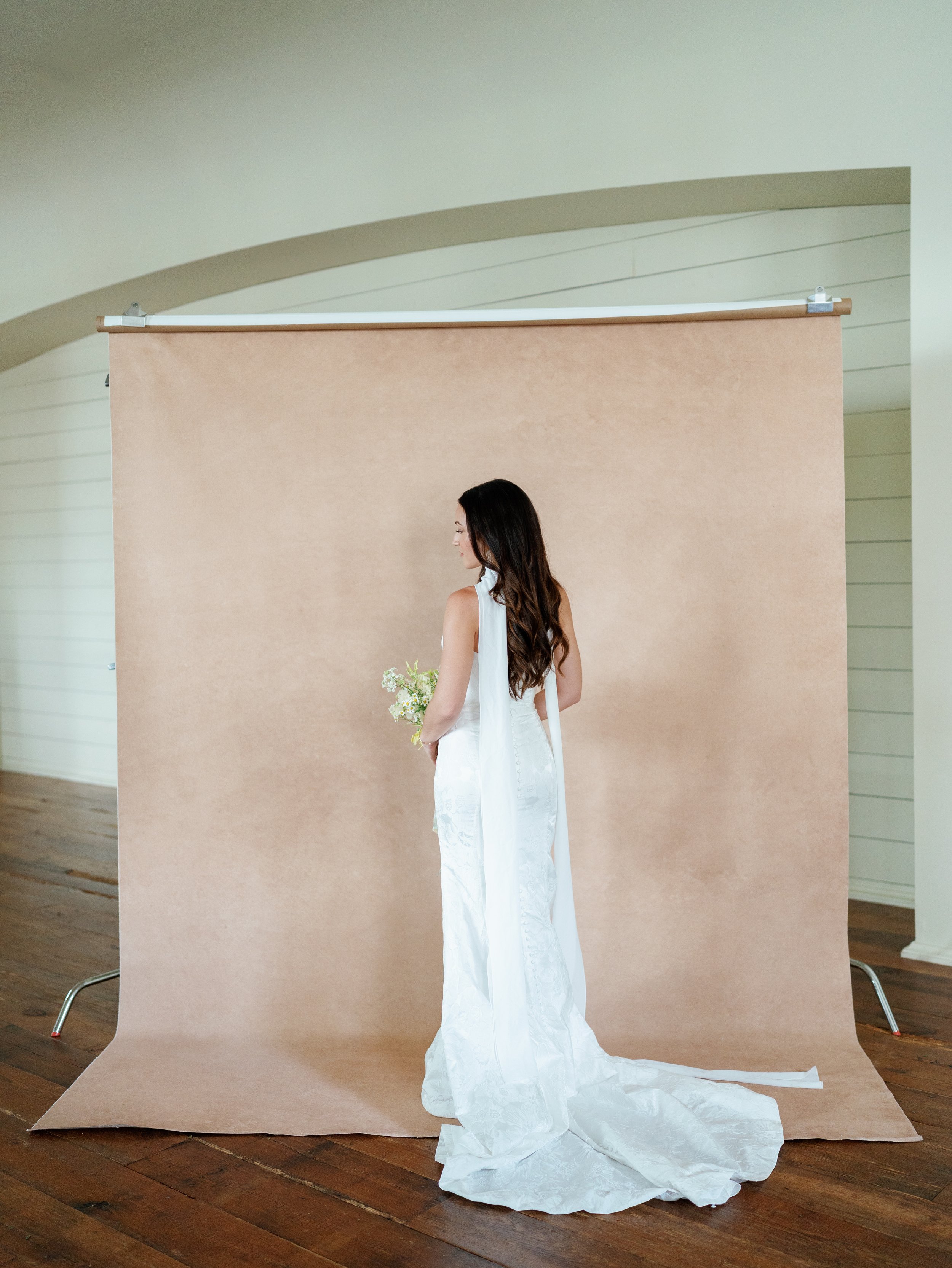 Full-length bridal portrait of a dark-haired bride in a white gown against a Chasing Stone Clay hand-painted canvas backdrop