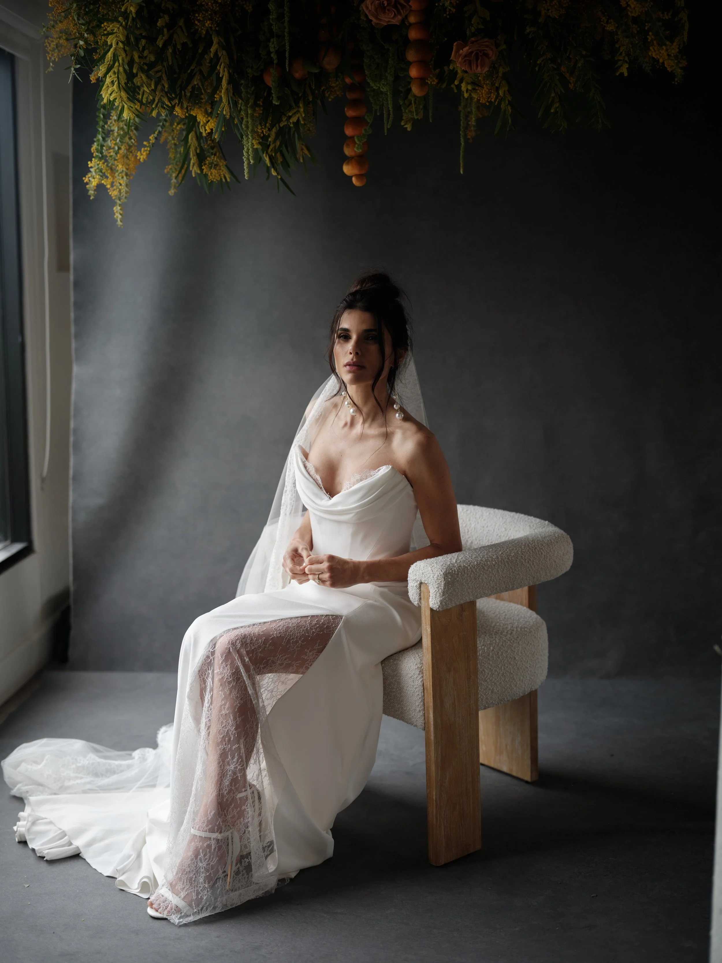 Editorial bridal portrait using Chasing Stone canvas backdrop, bride in strapless wedding dress with veil seated under dried floral hanging installation