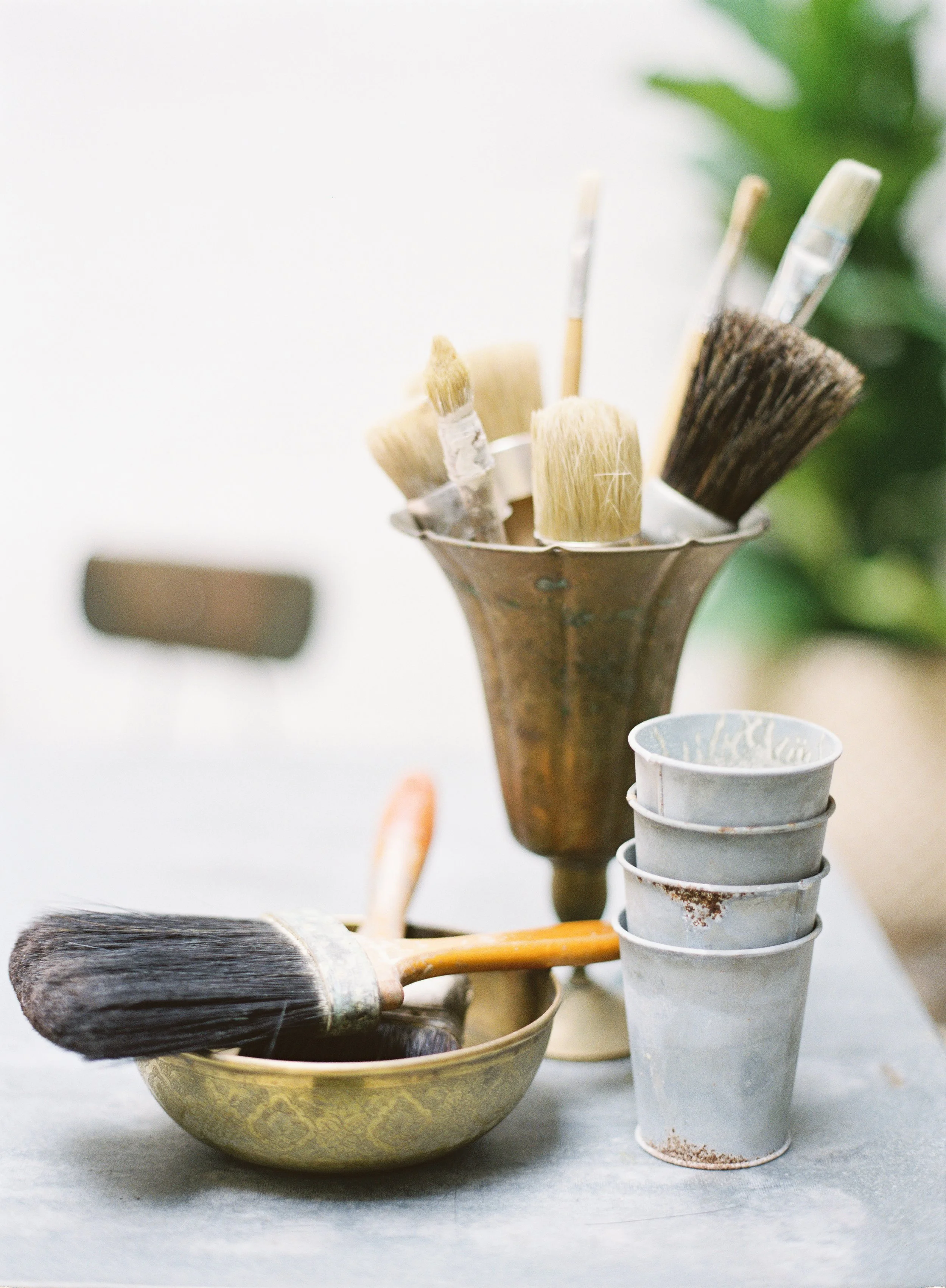 various painting brushes in vintage container with paint cups showing tools used to create hand-painted canvas backdrops