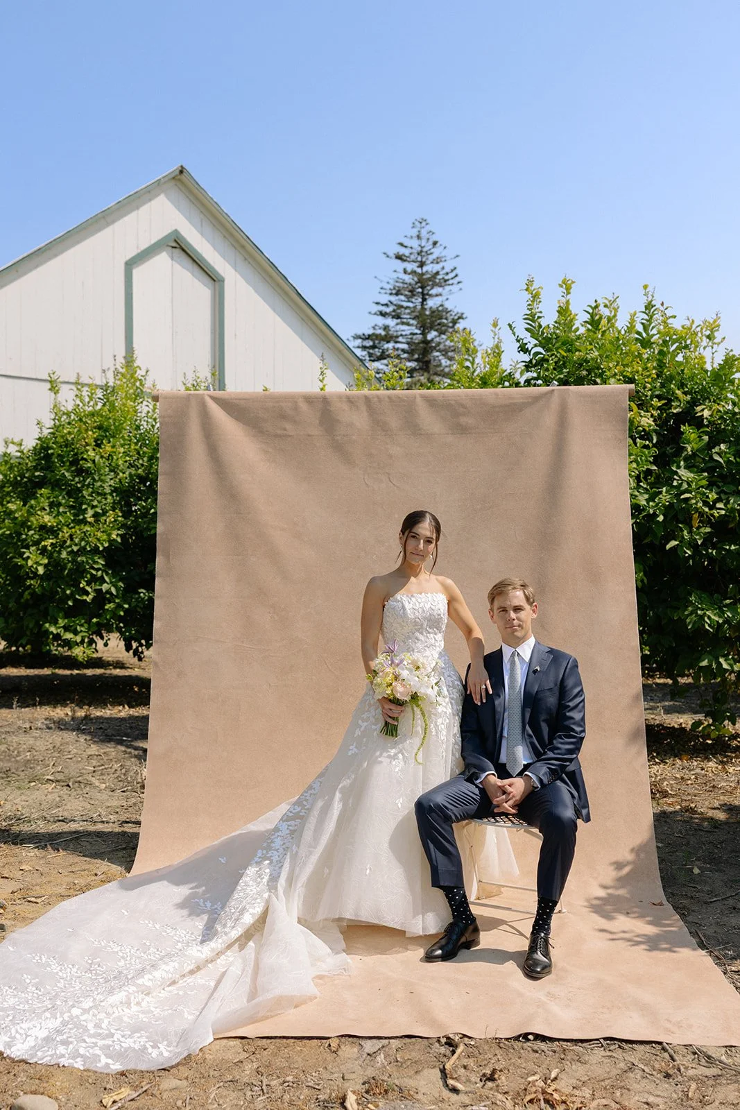 bride and groom portrait outdoors against a tan hand-painted canvas backdrop near a barn