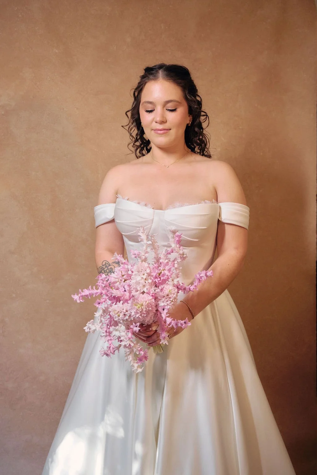 Bride holding pink bouquet in front of a warm Clay canvas backdrop lit with indoor golden hour studio lighting