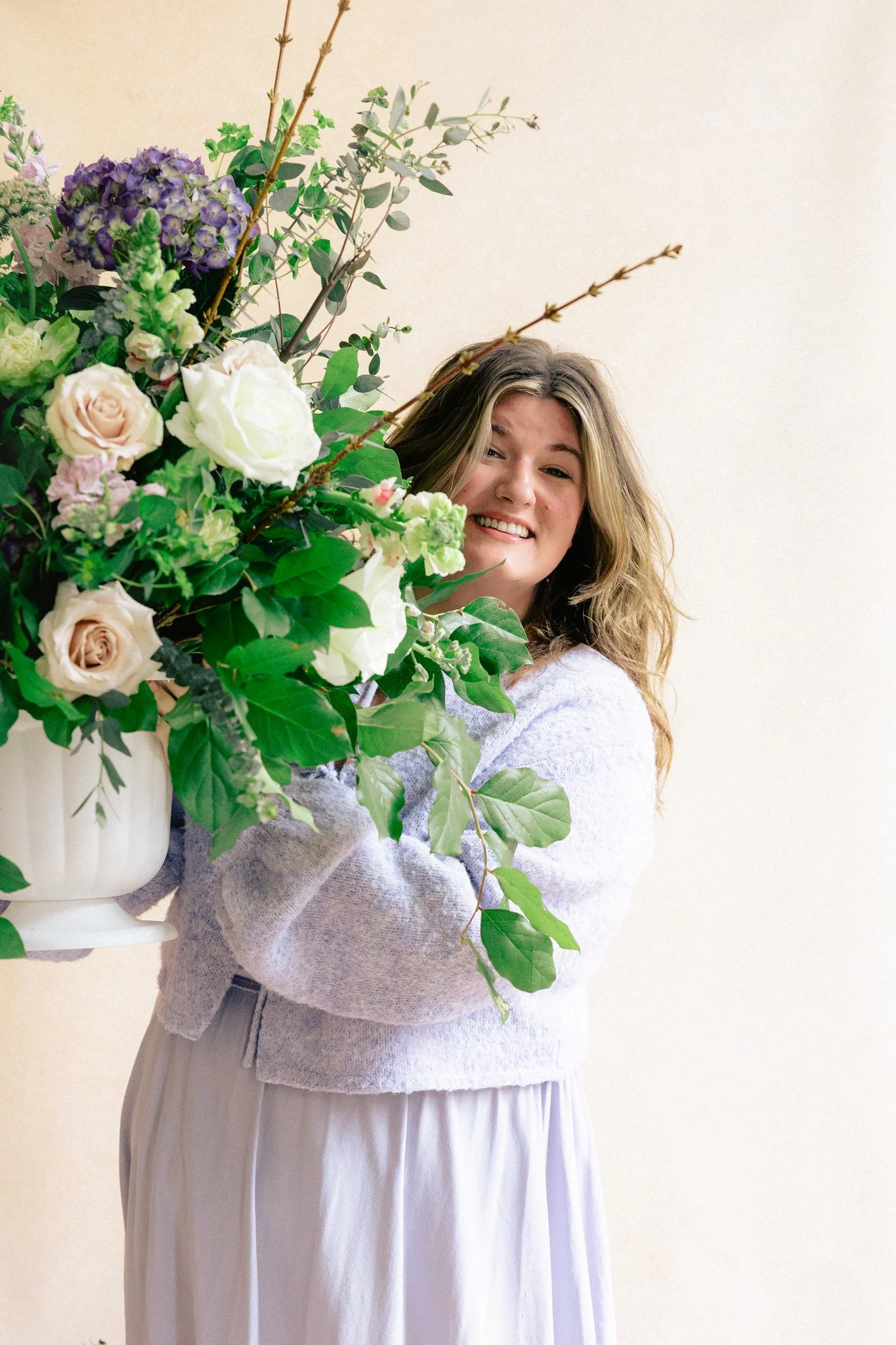 portrait of a woman holding a large floral arrangement in front of a hand-painted canvas photography backdrop with soft natural light and textured neutral tones
