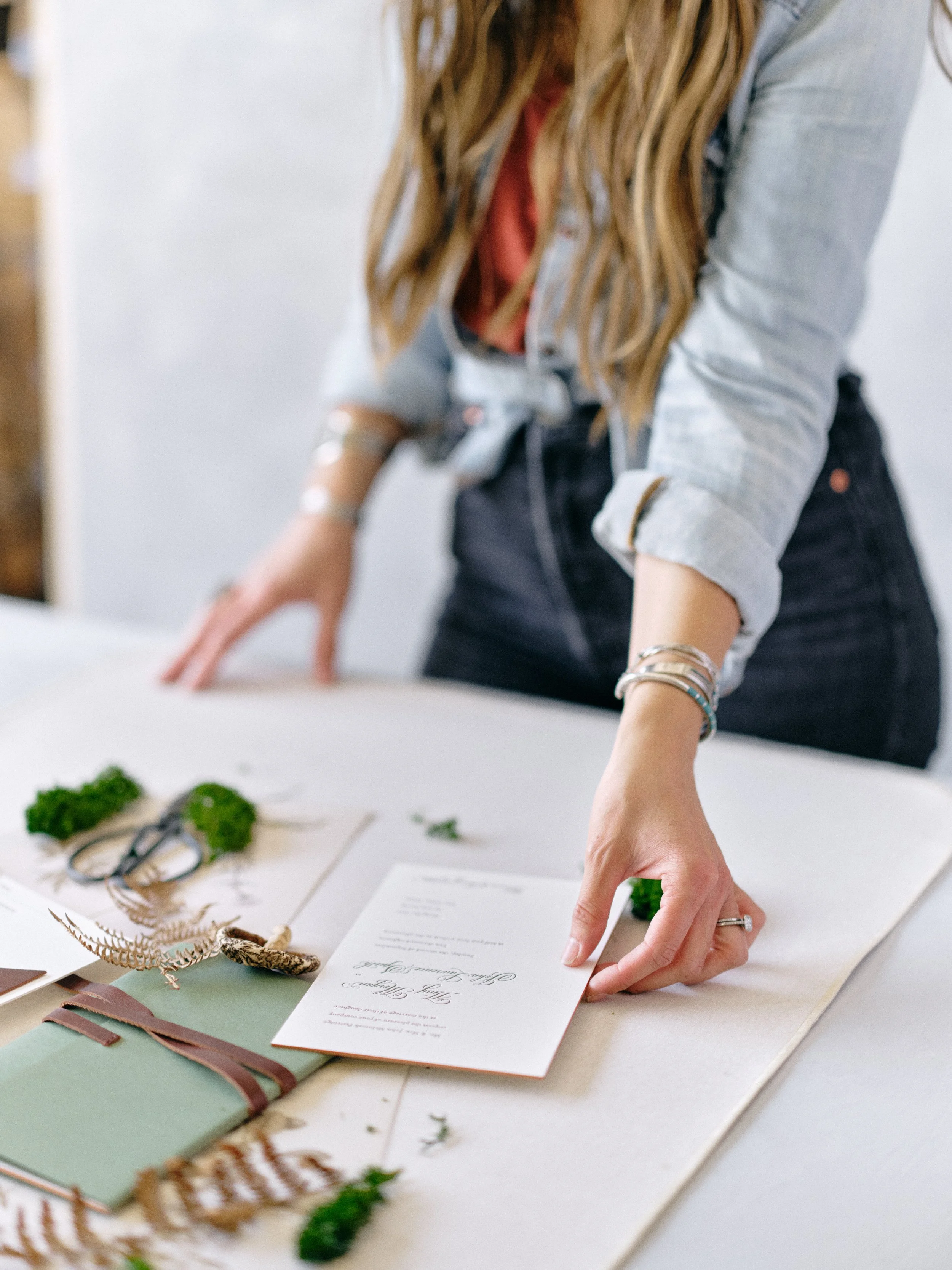 hands arranging invitation flat lay on canvas backdrop with natural styling elements