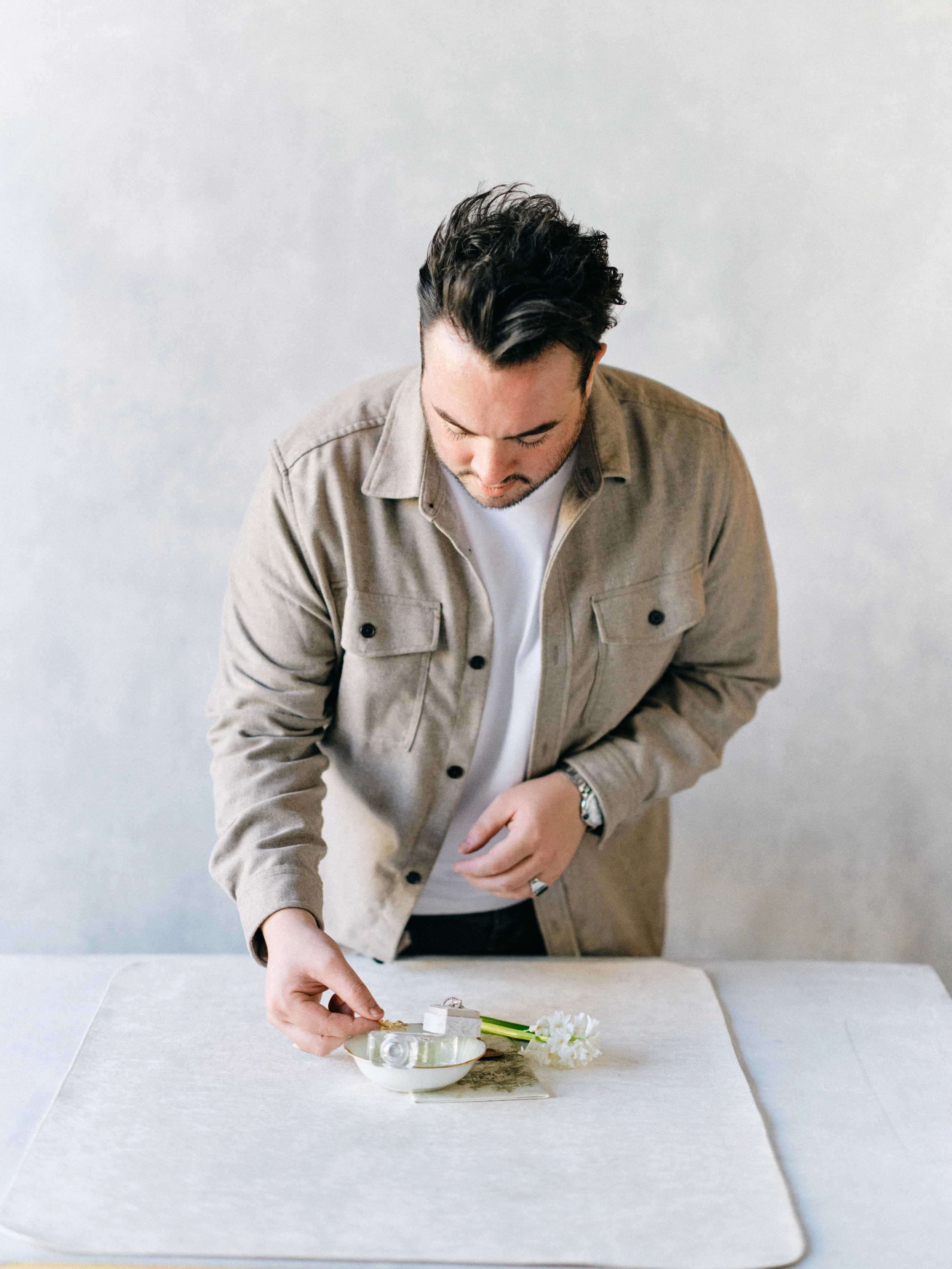Portrait subject in warm neutral clothing arranging a flat lay detail shot against a cool gray canvas backdrop