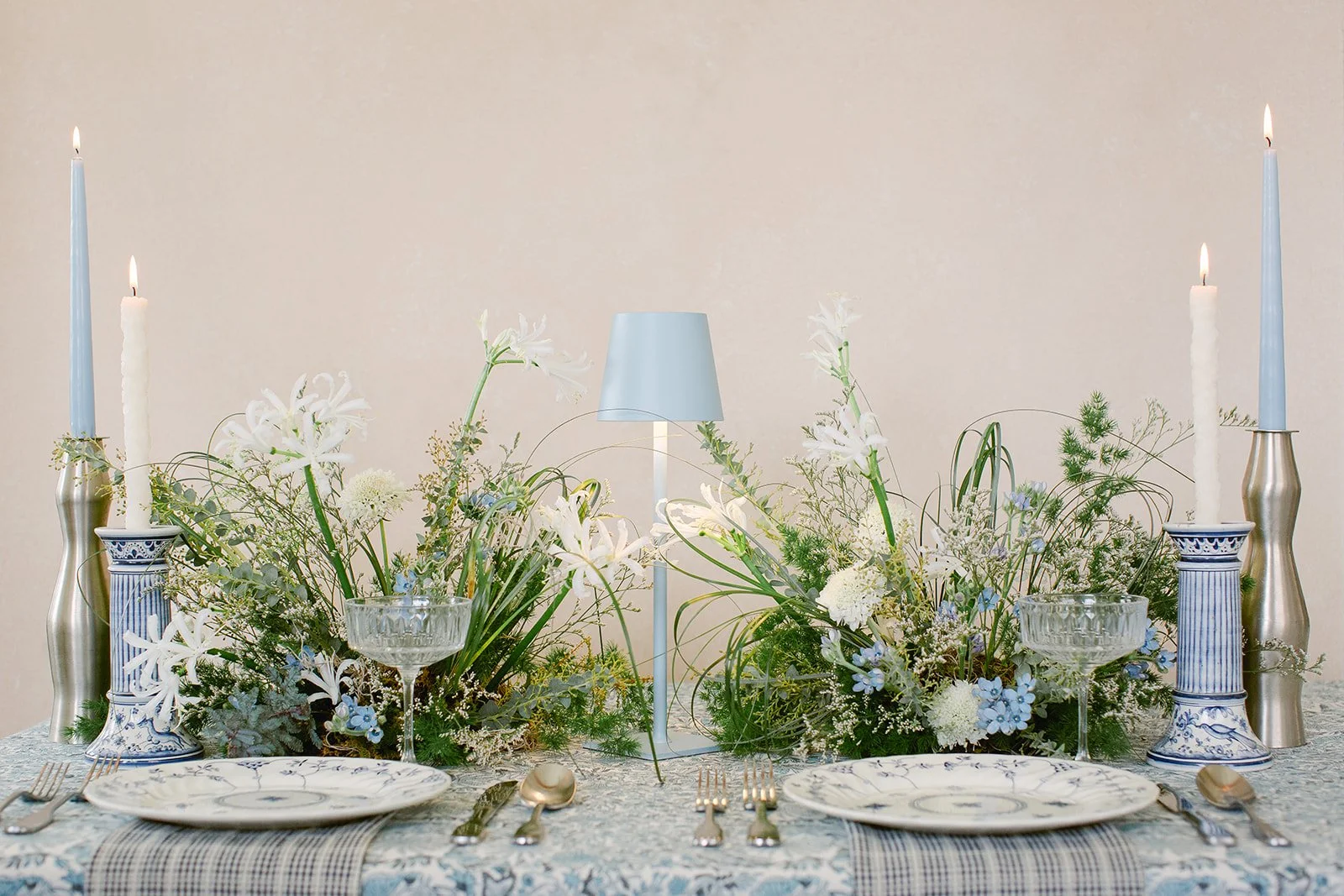 Editorial wedding tablescape with blue and white florals, candlelight, vintage-inspired china, and a hand-painted backdrop creating a soft luxury dining scene