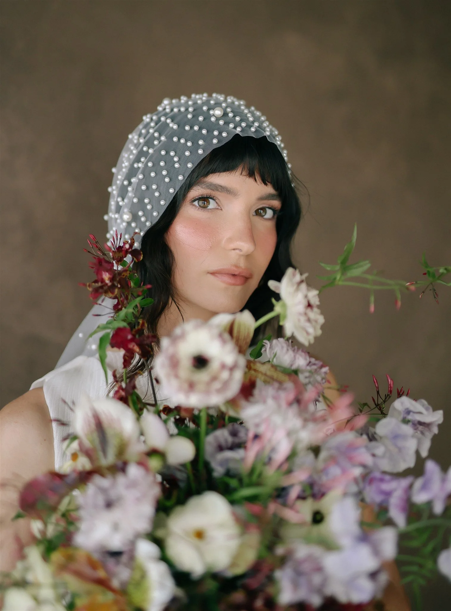 Editorial bridal portrait with pearl cap veil and floral bouquet against a Chasing Stone Umber hand-painted canvas backdrop