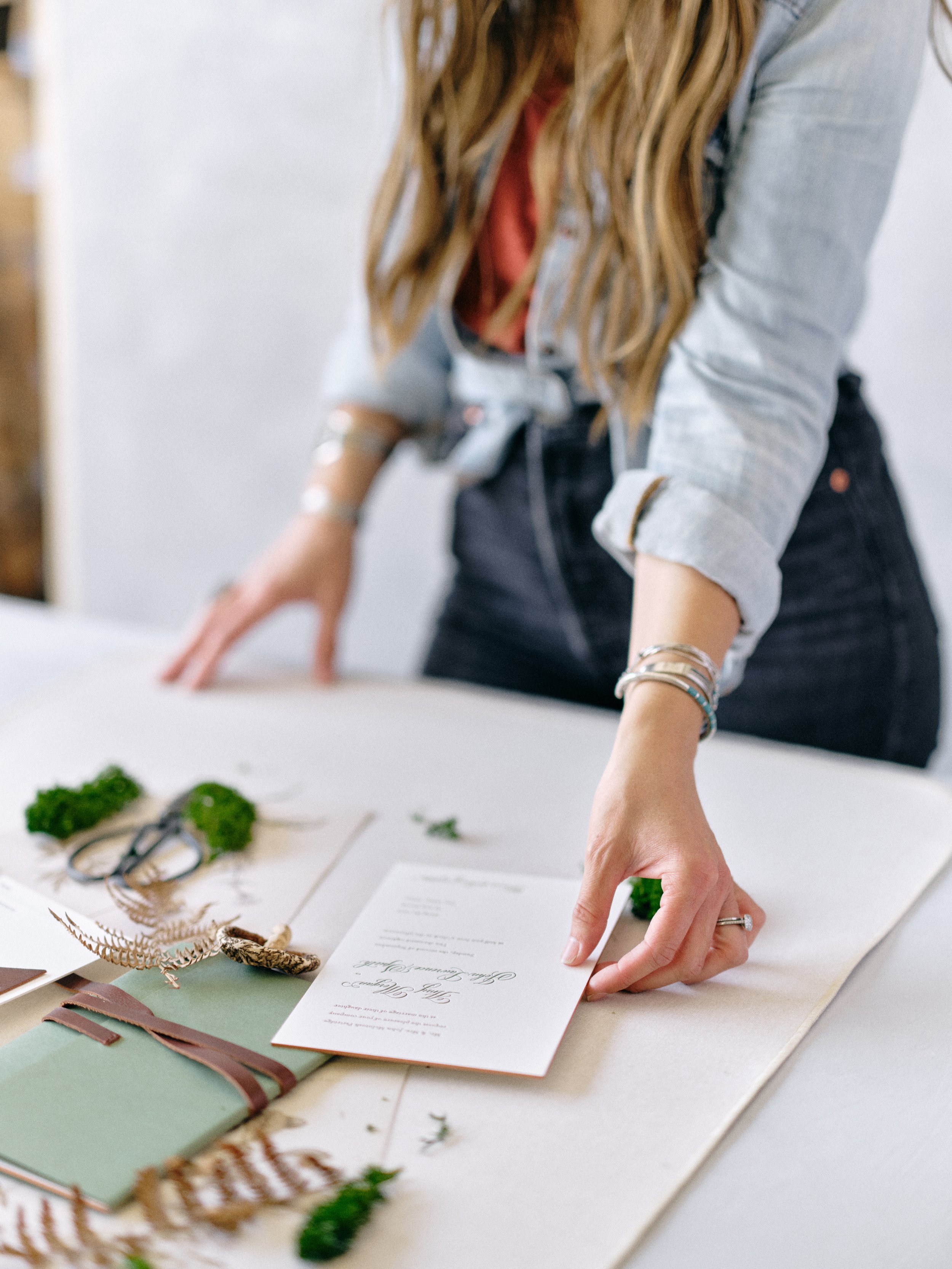 Wedding flat lay photography showing layered composition with invitation suite, vintage stamps, velvet ribbon, and florals on yarrow blue-gray styling surface
