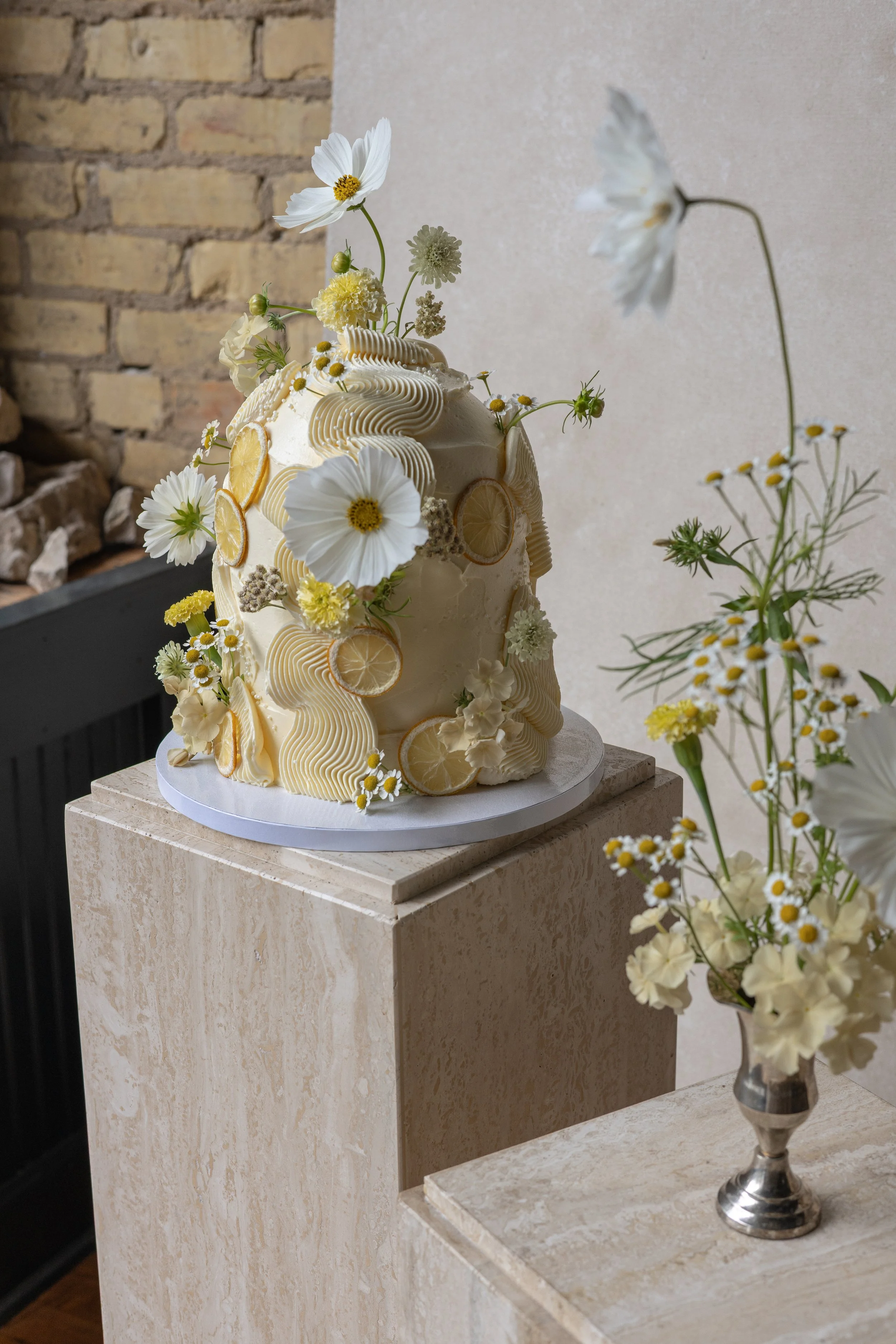 Styled lemon floral cake photographed on a pedestal with a textured hand-painted backdrop in a small home studio