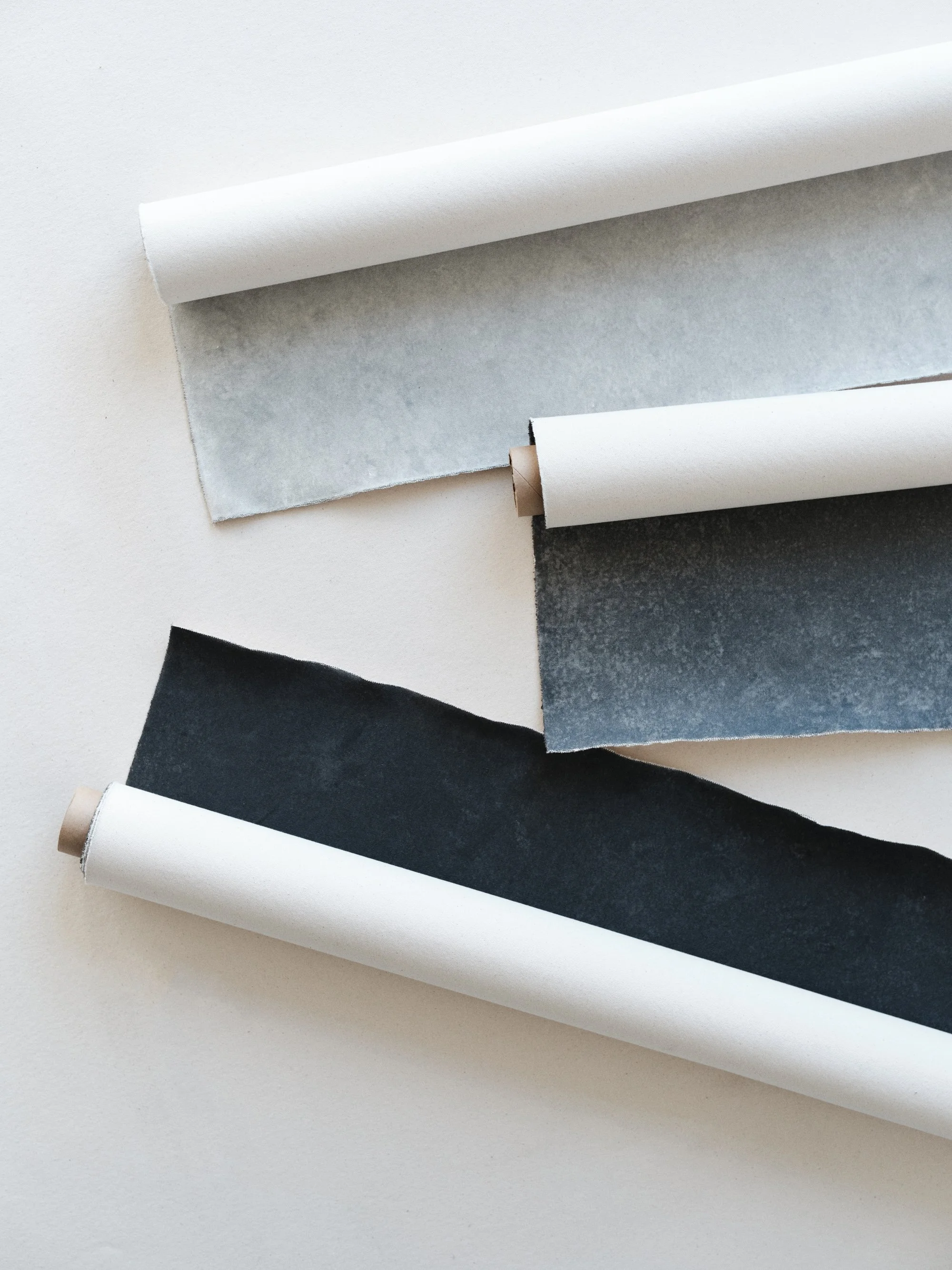 Three complementary hand-painted photography backdrops in cool gray tones - Graphite, Slate, and Carbon - rolled and layered to show color palette cohesion