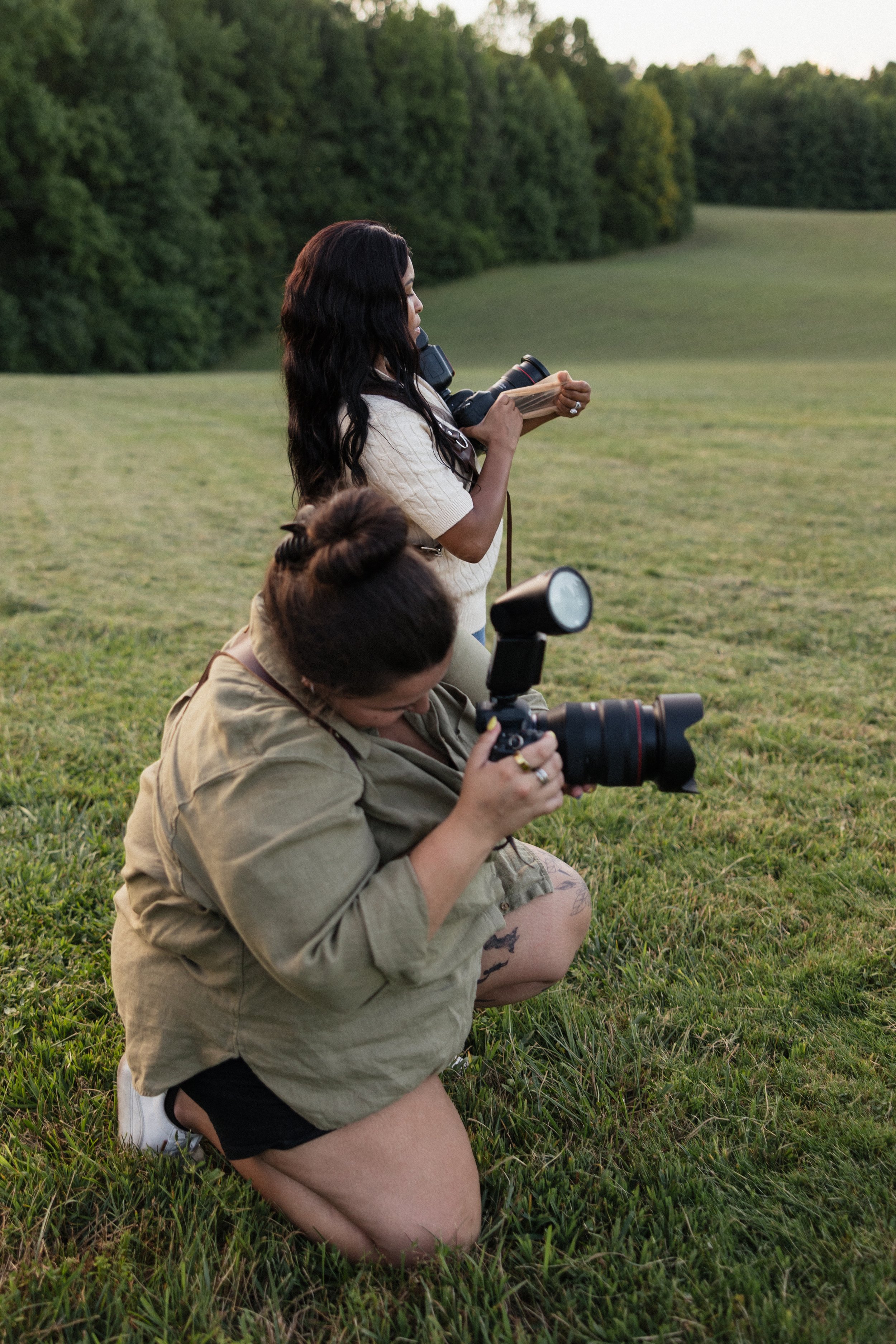 two photographers reviewing a portrait shot on camera during an outdoor session in a grassy field at golden hour