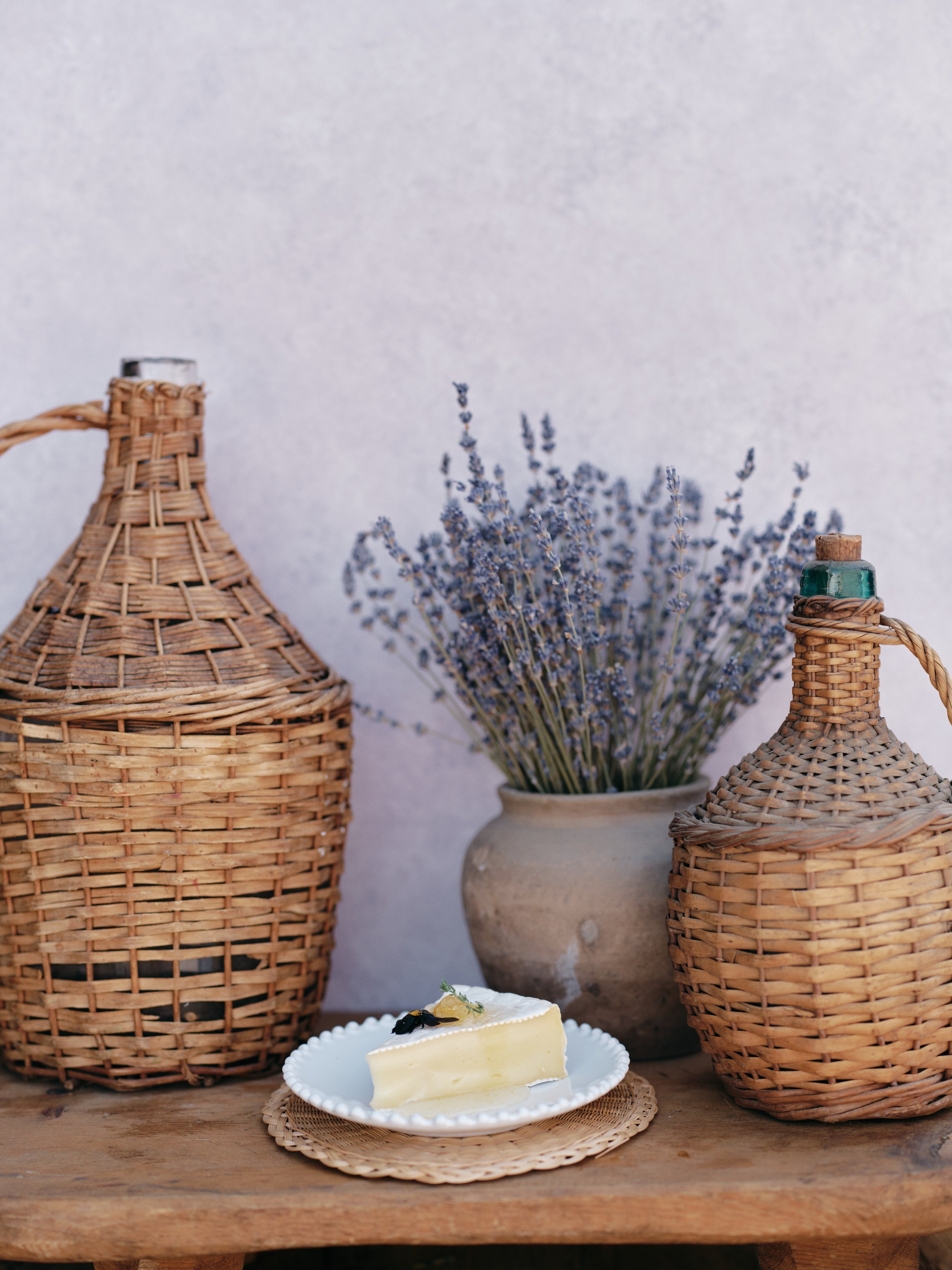 hand-painted textured backdrop in soft lavender showing rustic wicker bottles, dried lavender, and dessert styling demonstrating how real texture creates depth in product photography