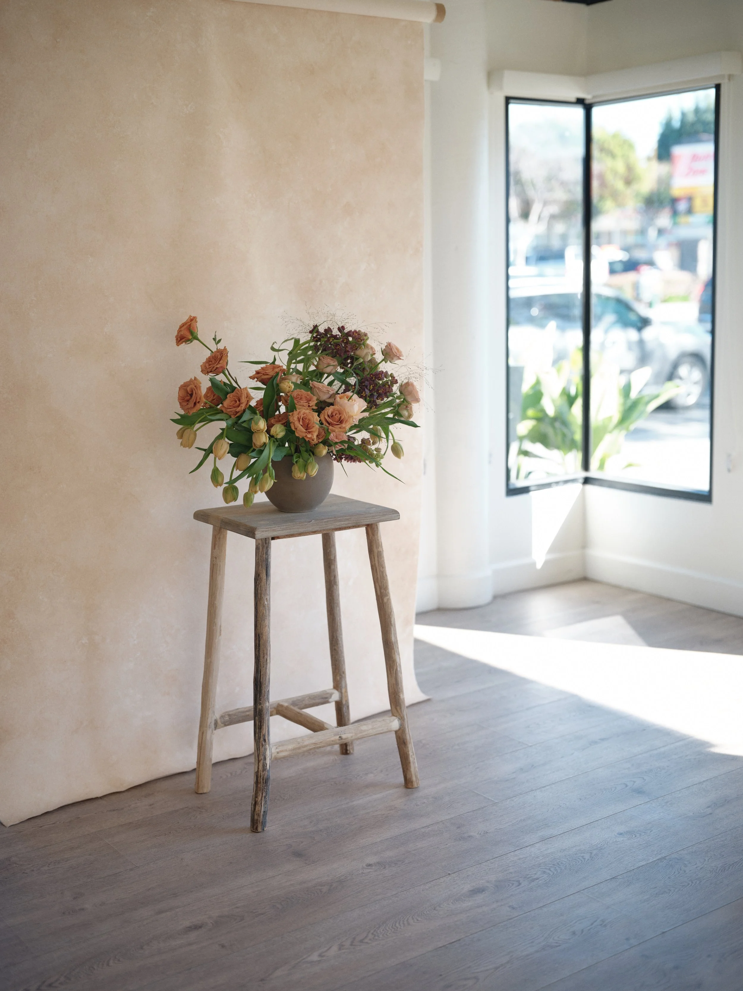 Sandstone warm neutral hand-painted canvas backdrop in natural light showing authentic texture and dimension with analogous warm floral palette demonstrating superiority over printed backdrops