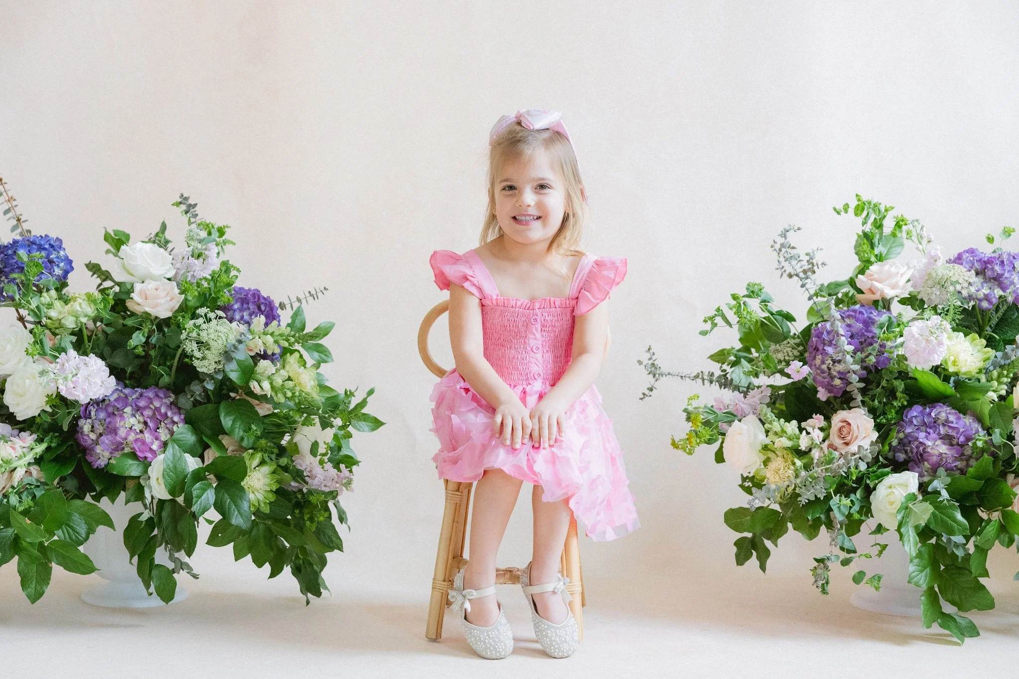 young girl in a pink dress seated between floral arrangements in front of a Chasing Stone Limestone hand-painted canvas backdrop