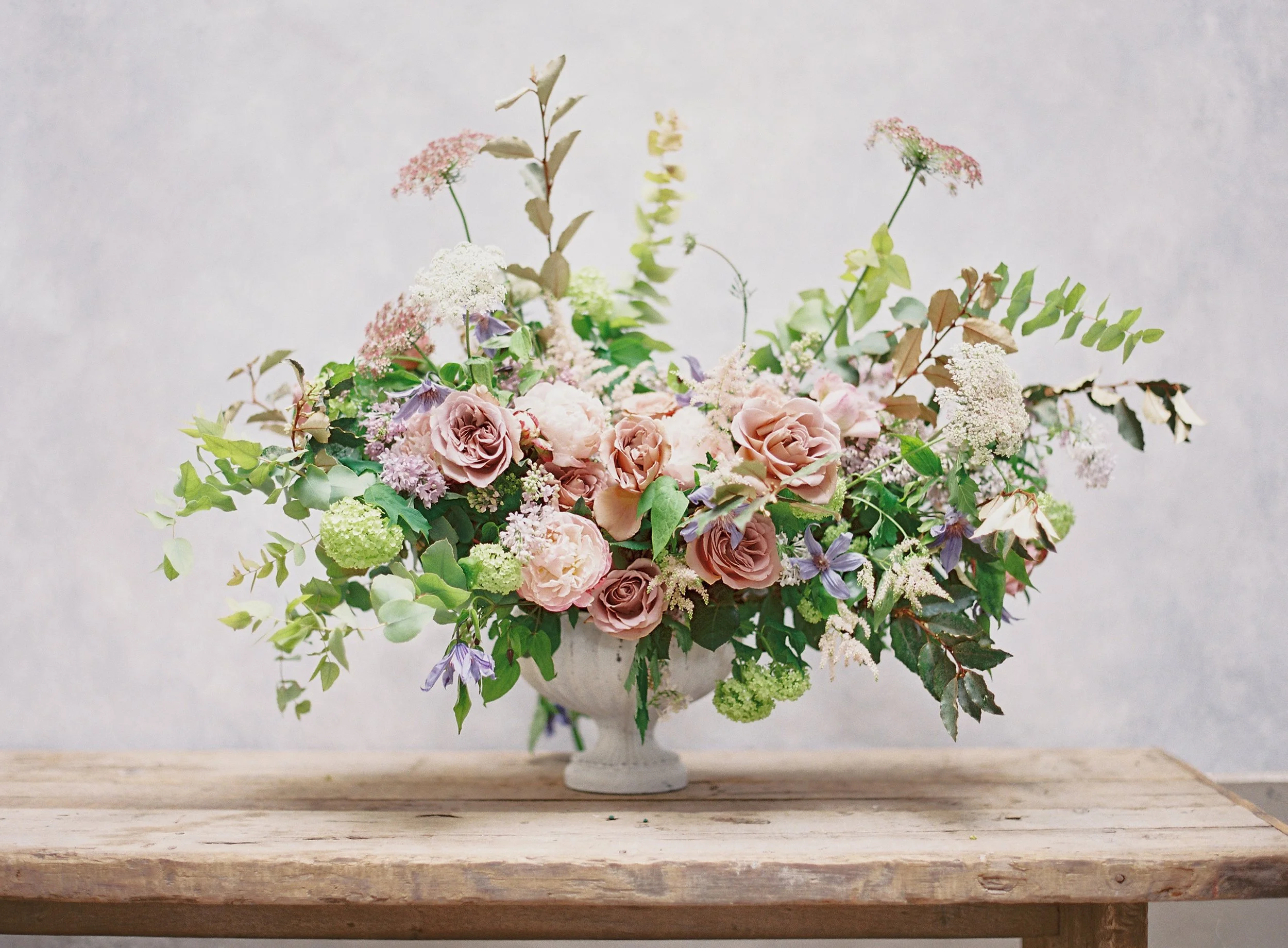 wedding floral photography on warm neutral taupe backdrop showing analogous color palette with blush roses, purple accents, and green foliage demonstrating color theory for photographers