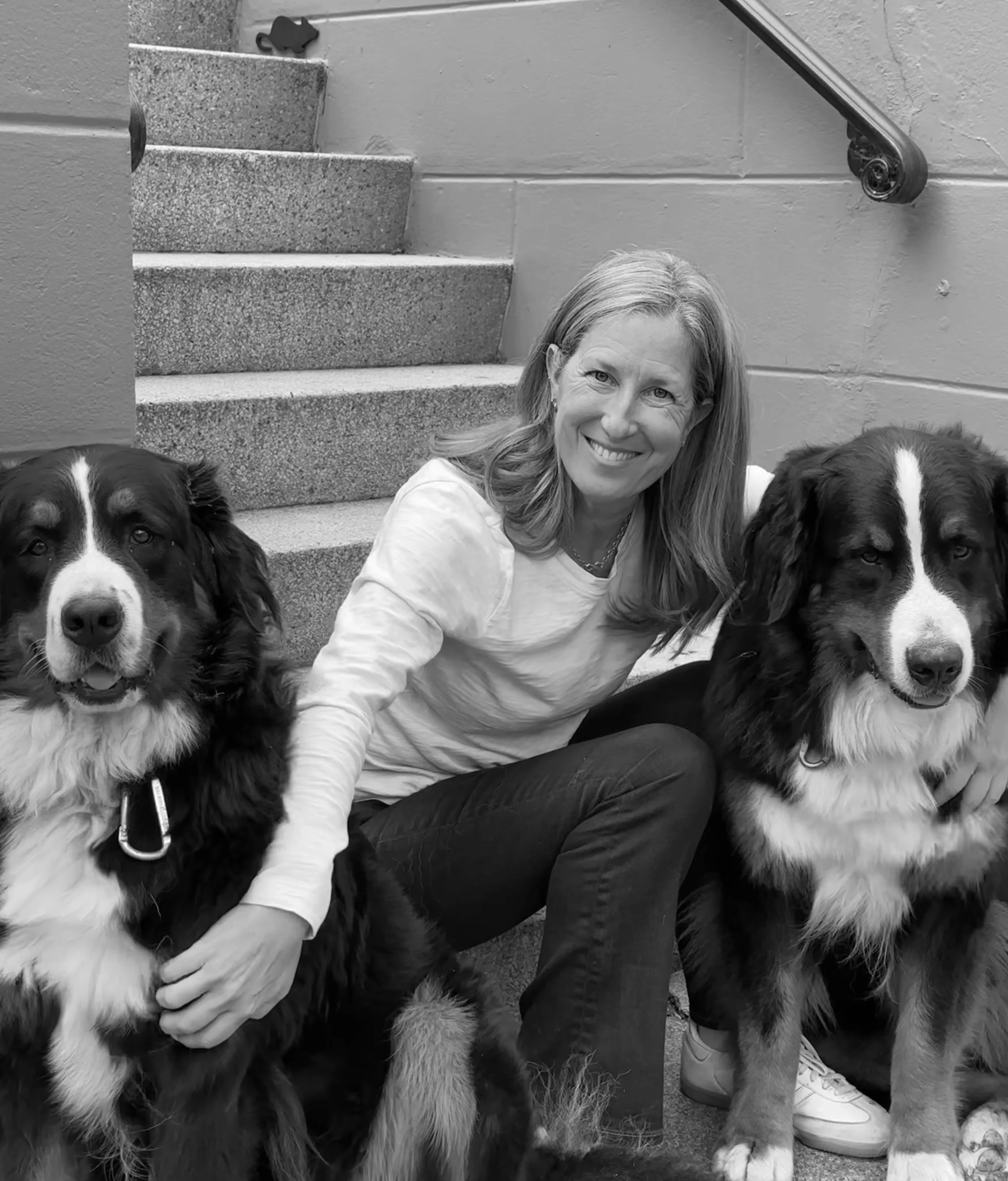Sondra Cluer, founder of Napa Bloom, sitting on steps with two Bernese Mountain Dogs, black-and-white photo