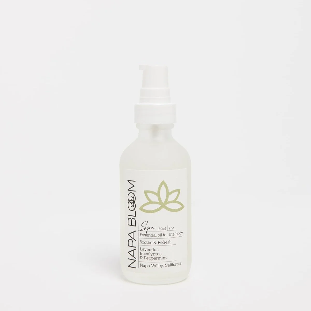 Napa Bloom Spa Body Oil in a 2 oz frosted glass travel-size bottle with white pump and ivory label featuring a green lotus design — eucalyptus, peppermint, and lavender blend.