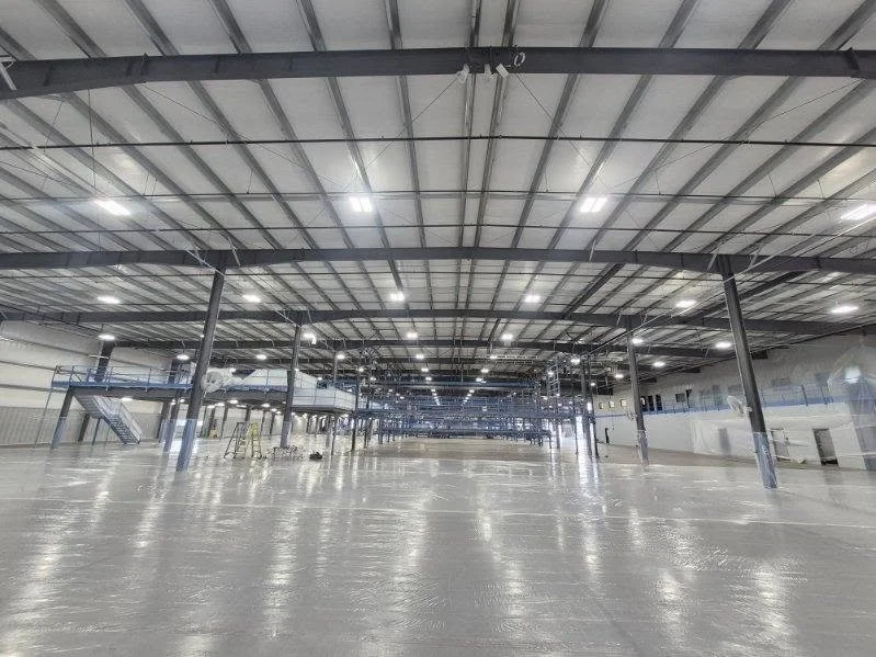 Wide industrial interior with metal roof framing and evenly spaced support columns.