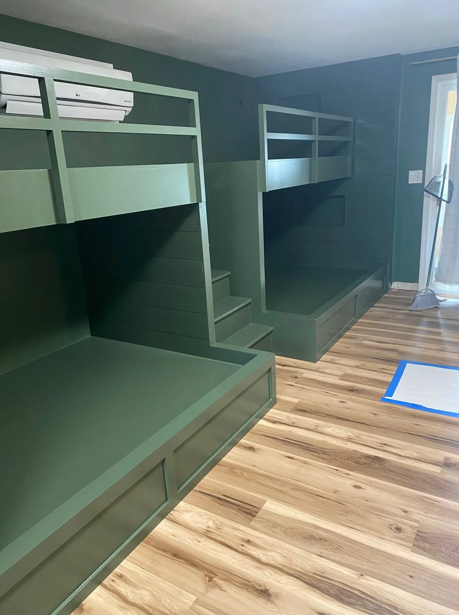 Side view of green built-in bunk beds with a ladder and wood flooring.