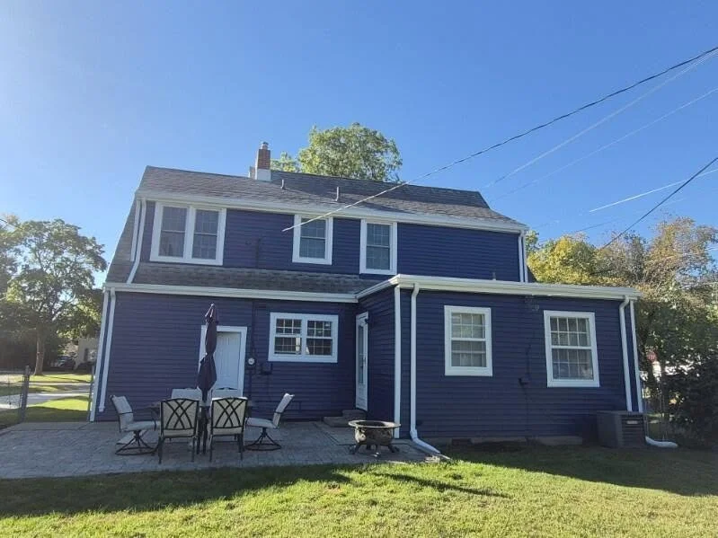 Patio side of a blue home with white window trim and gutters.
