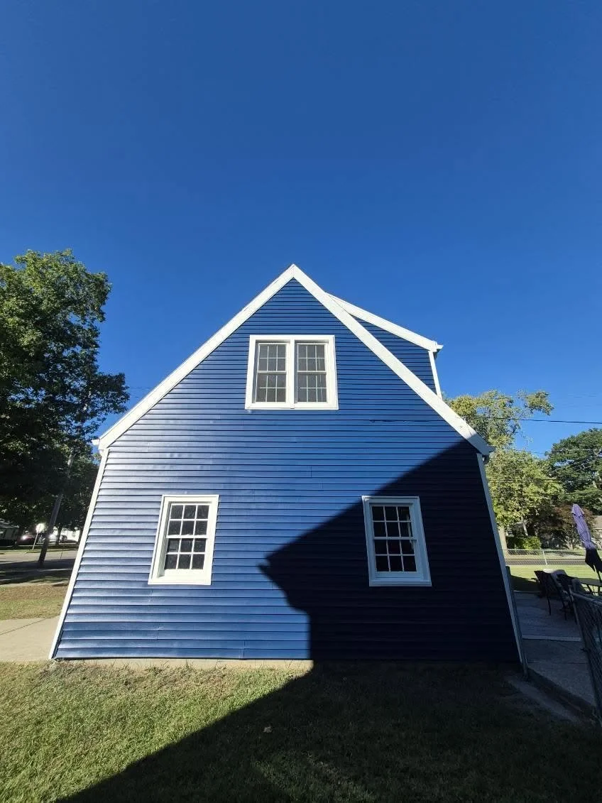 Gabled side of a blue home with white window and roof trim.