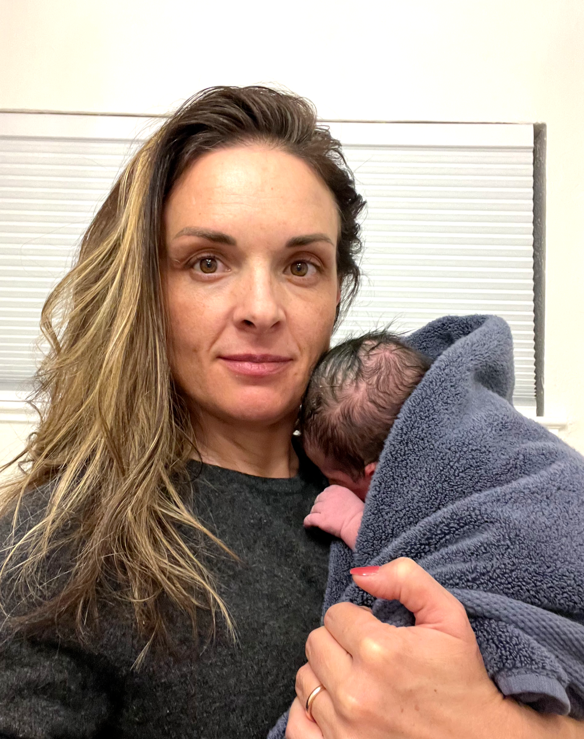 A woman with long wavy hair holding a newborn baby wrapped in a blue blanket.