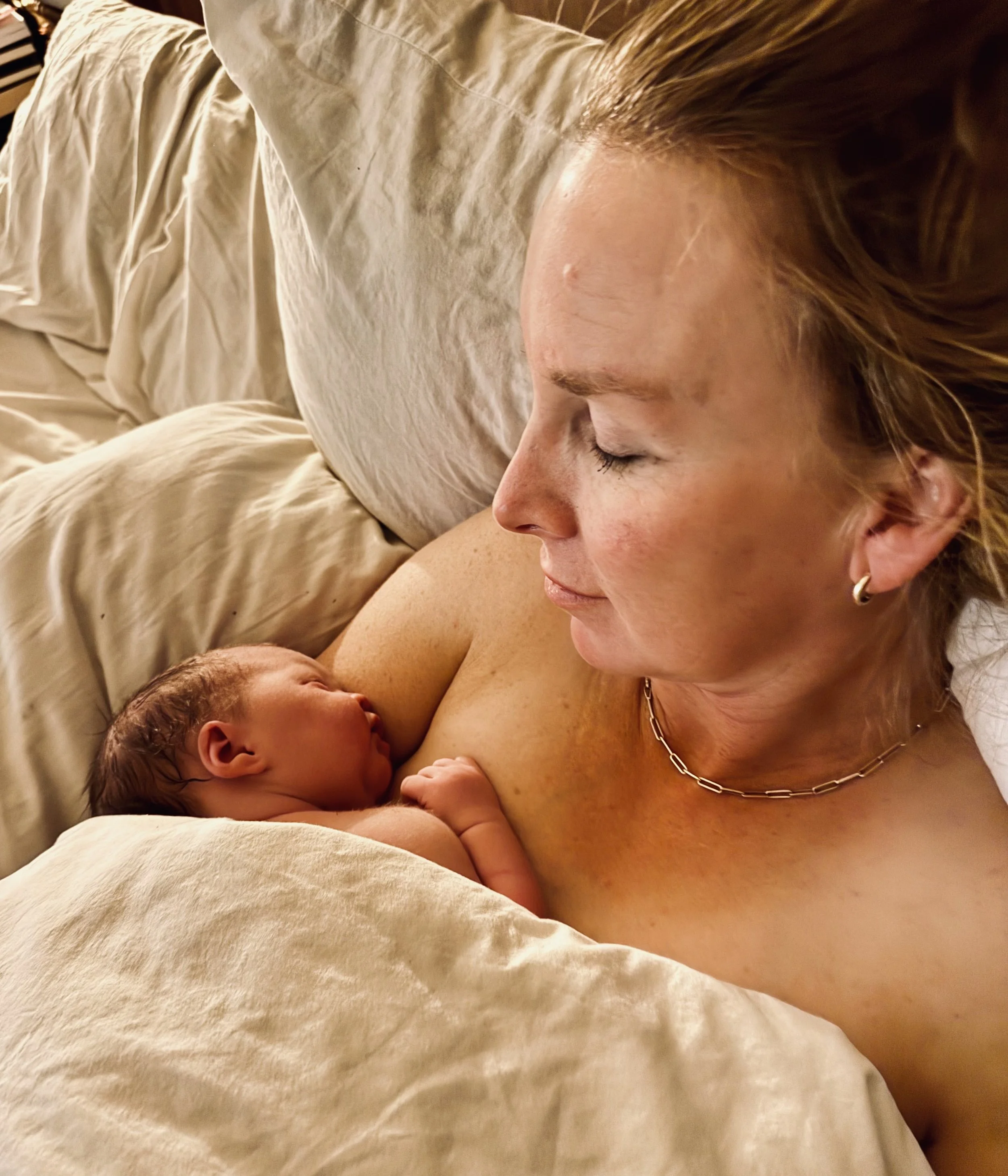 Woman holding a sleeping baby on her chest, both wrapped in a white blanket.