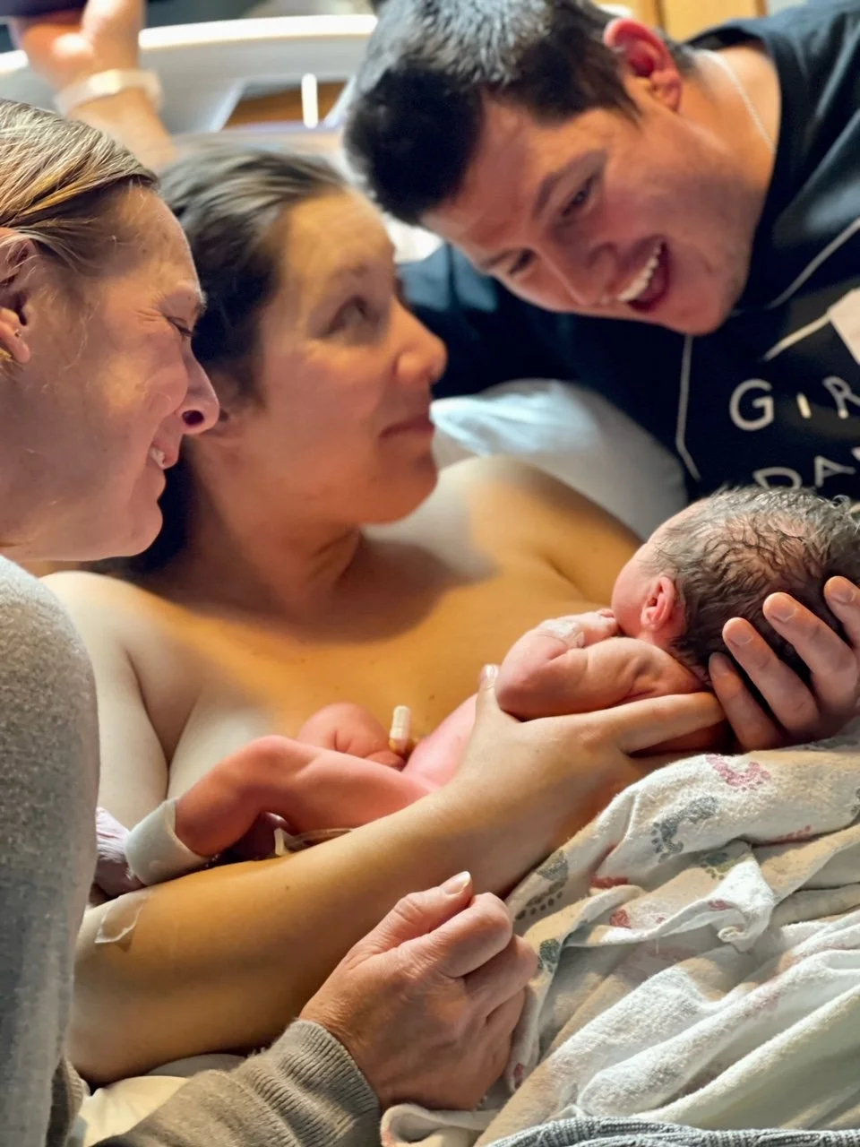 Parents and a medical staff member admiring a newborn baby in a hospital room.