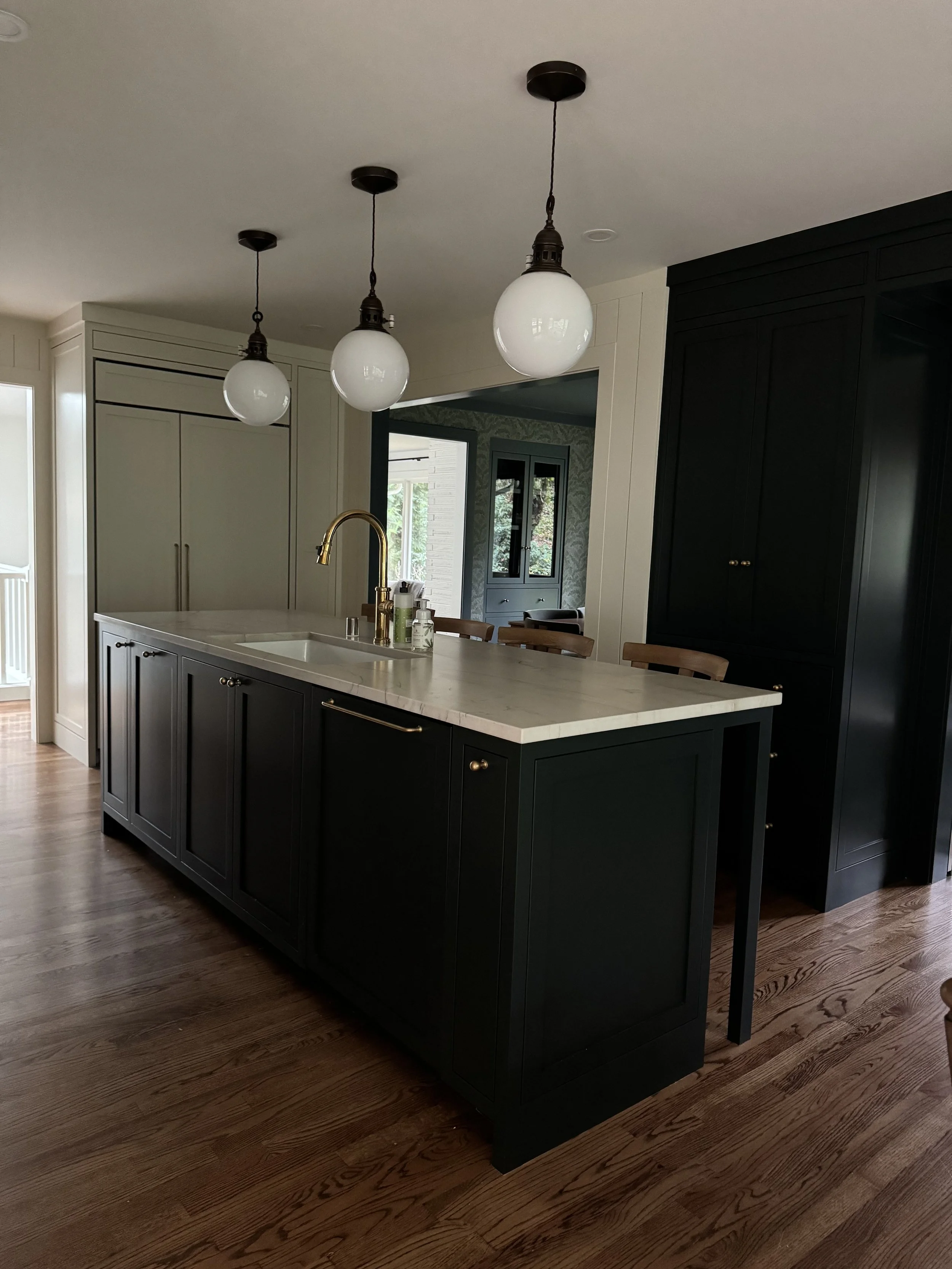 A modern kitchen with black cabinets, a marble island, and three hanging globe pendant lights.