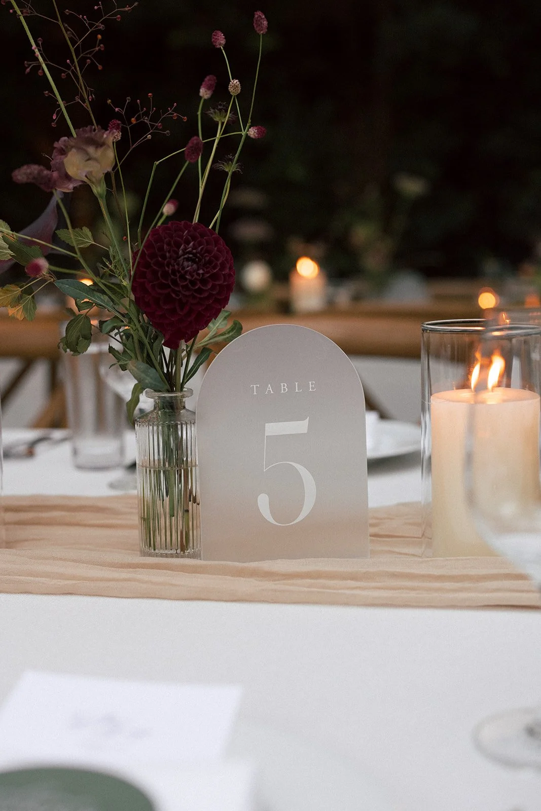 Table number 5 with a floral centerpiece and candle on a wedding reception table.