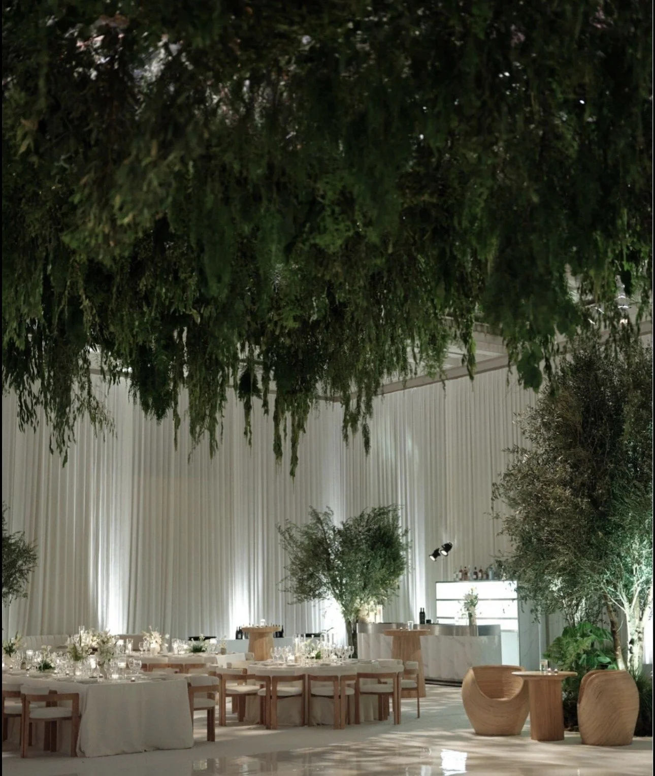 Elegant event space with white drapery, greenery, and wooden furniture set up for a formal gathering or celebration.