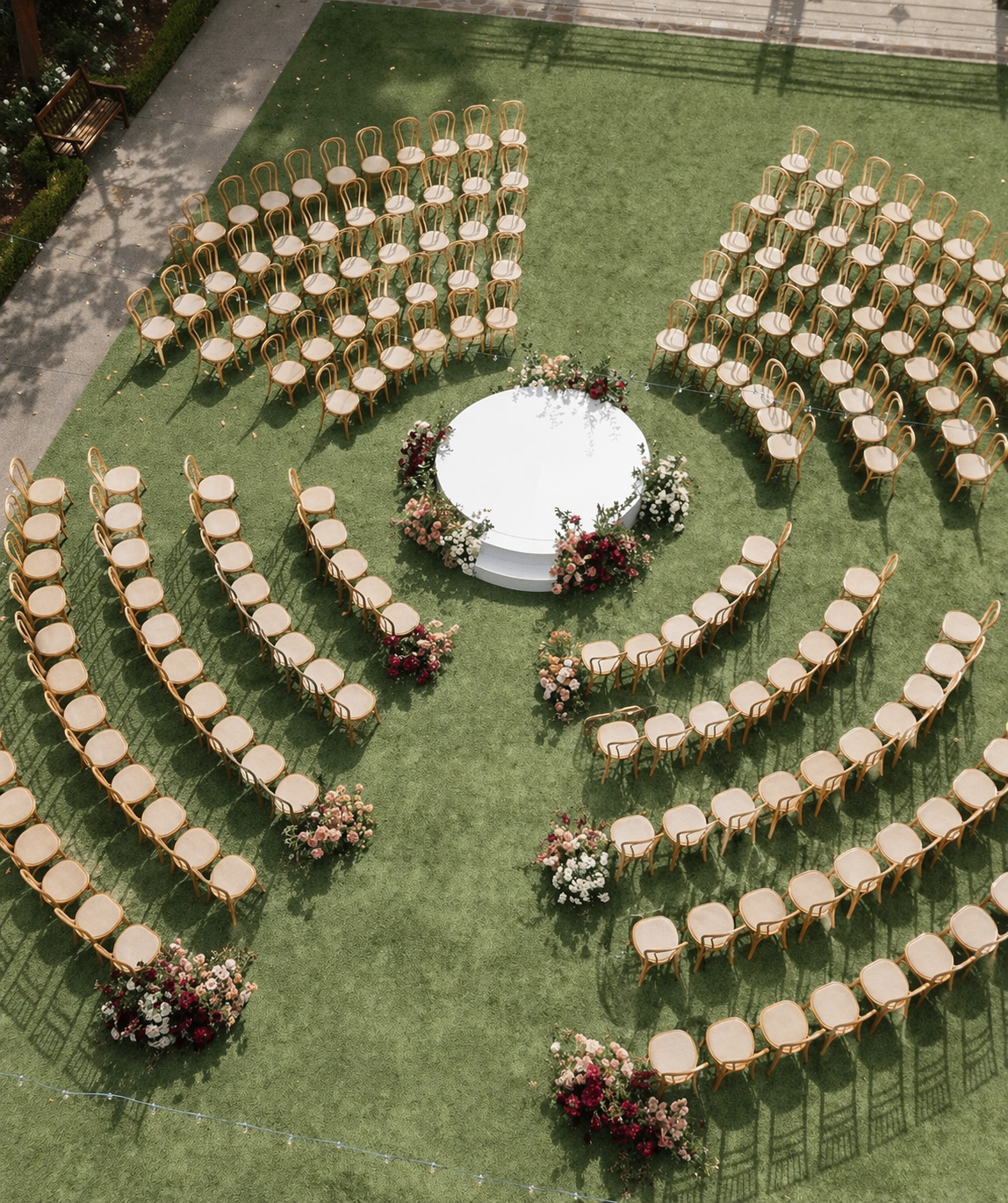 Empty chairs arranged in a semi-circular pattern around a round floral decorated platform on green grass for an outdoor wedding.