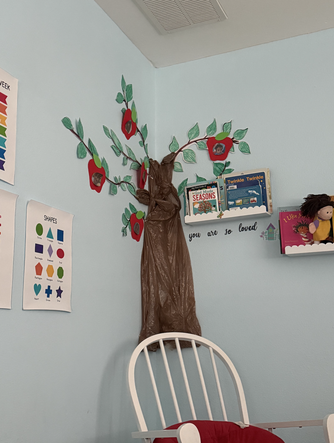 Decorative paper tree with green leaves and red apple-shaped photos on a light blue wall in a children's room.