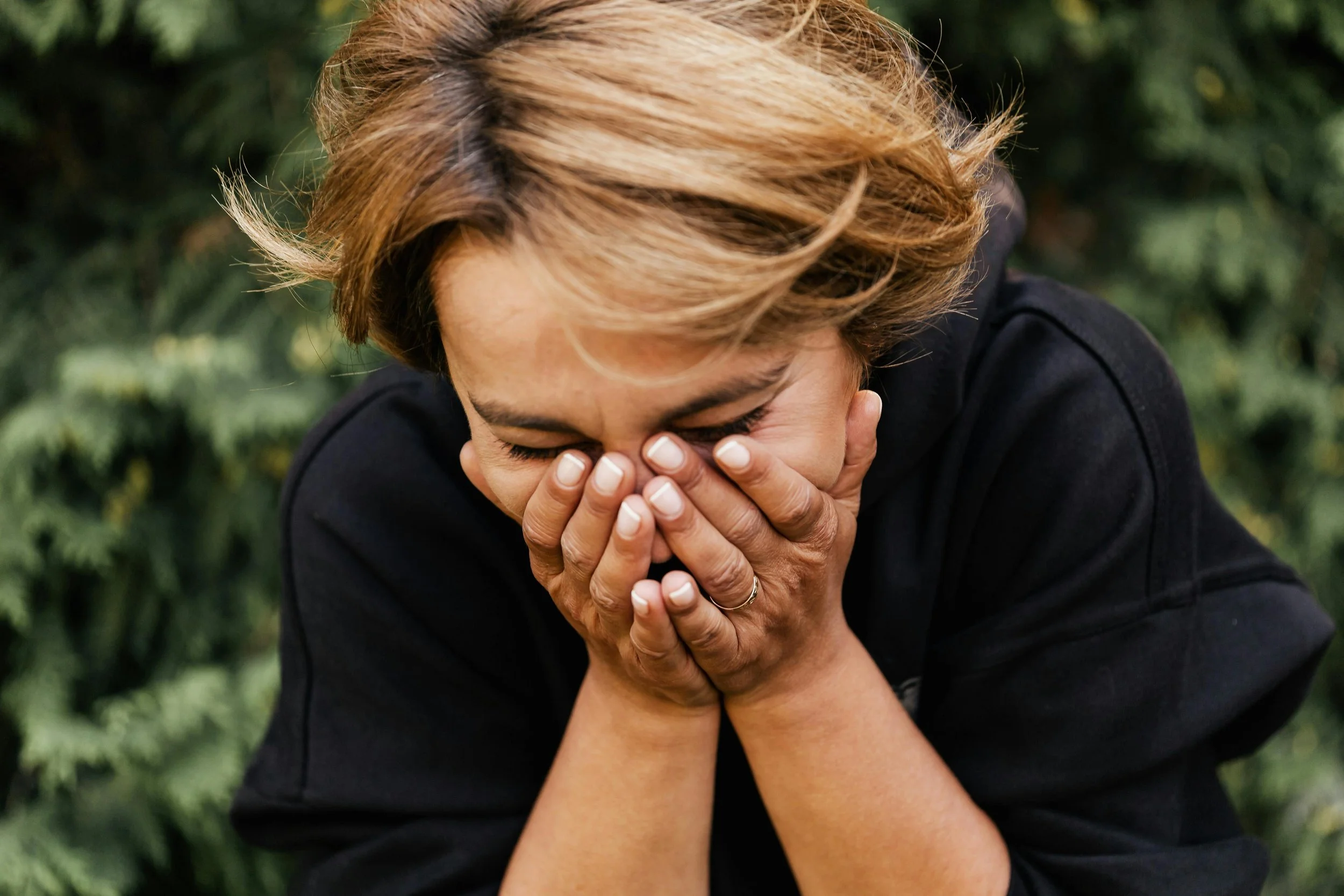 A woman outdoors with her face in her hands, overwhelmed by emotion — representing the courage it takes to face trauma and begin trauma therapy in Los Angeles, CA. 