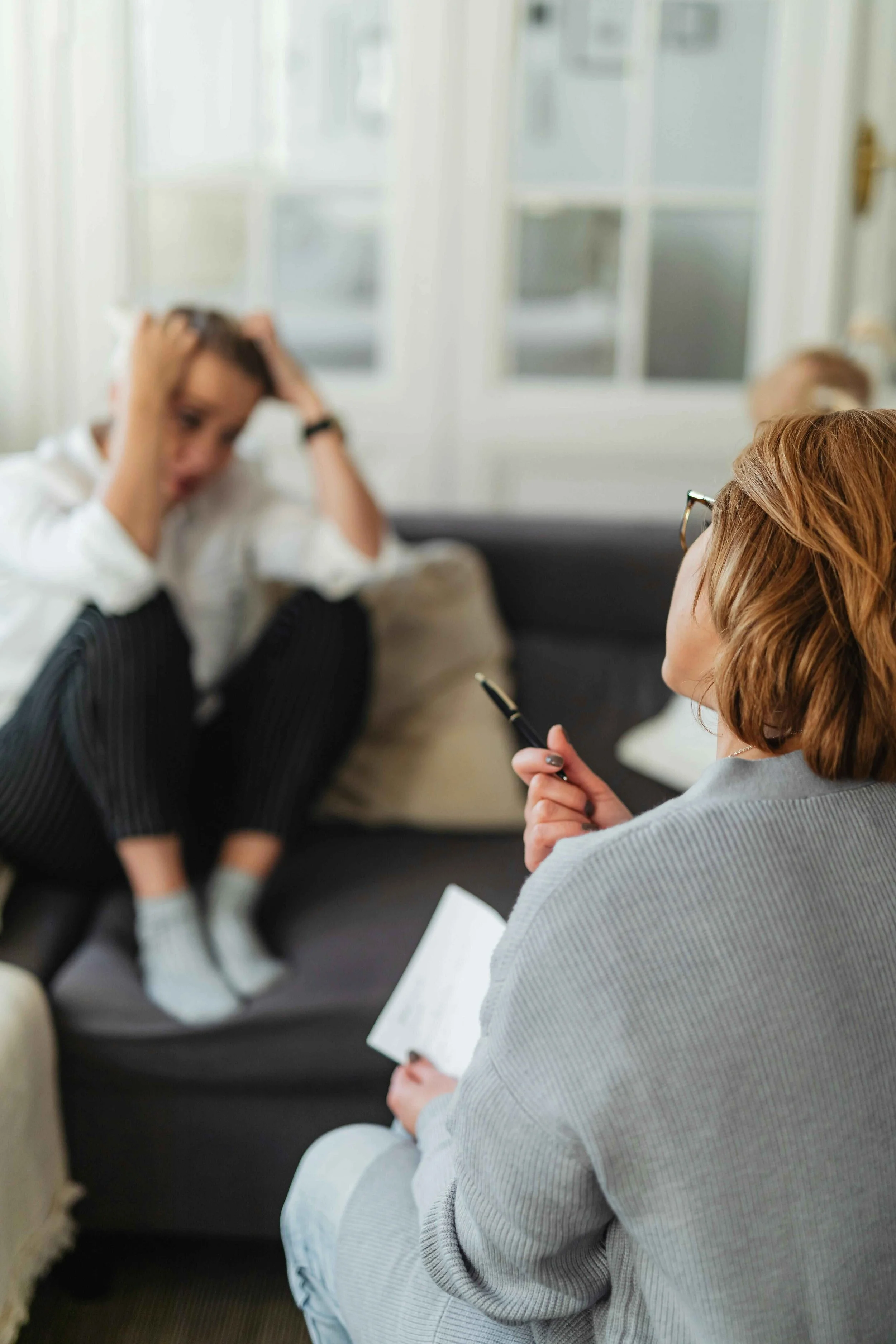 > A therapist seen from behind taking notes while a client sits across from her in a therapy session, representing inclusive and affirming therapy that honors every person's full identity in Los Angeles, CA.