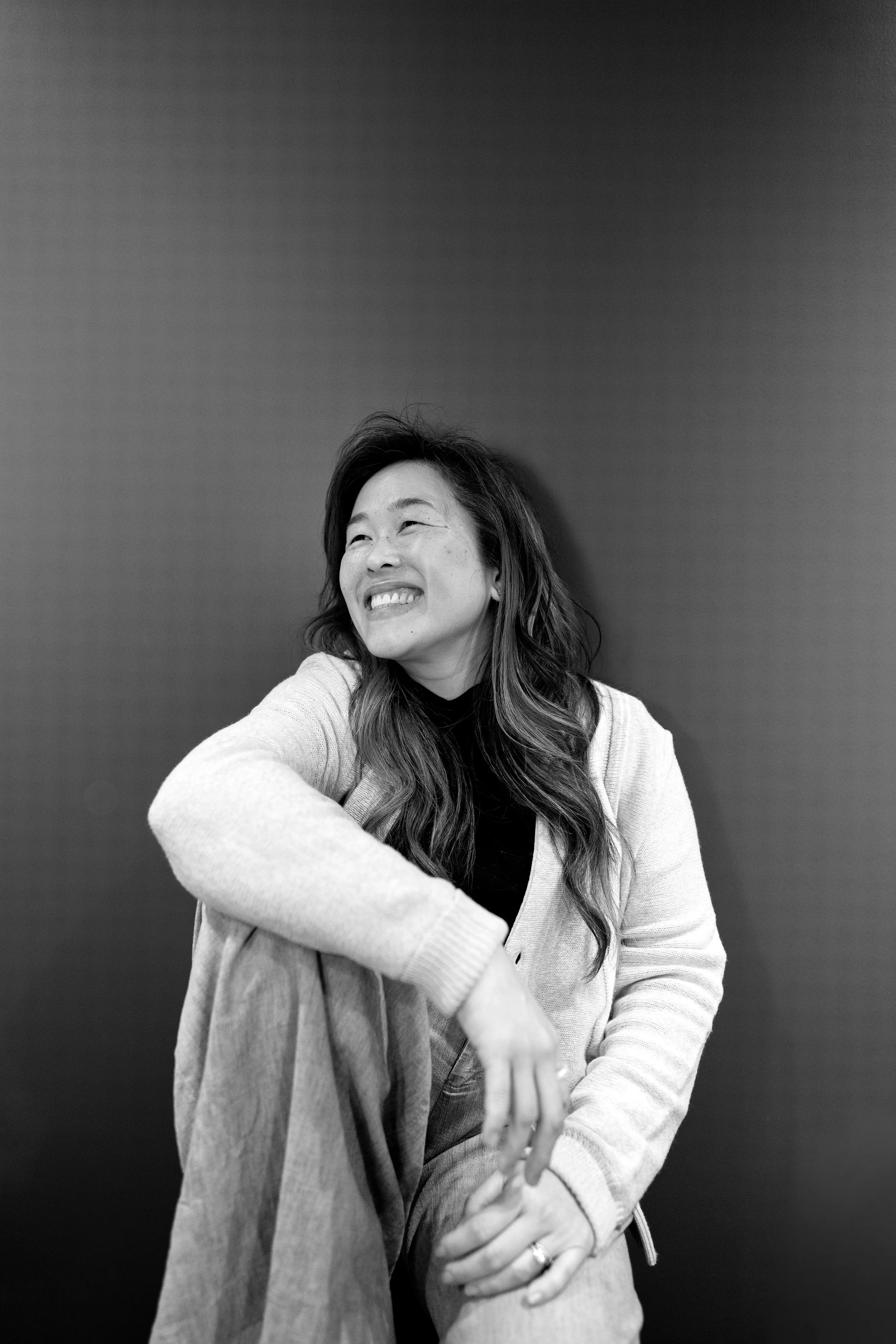 Black and white photo of a smiling woman with medium-length hair, wearing a dark shirt, looking to the side.