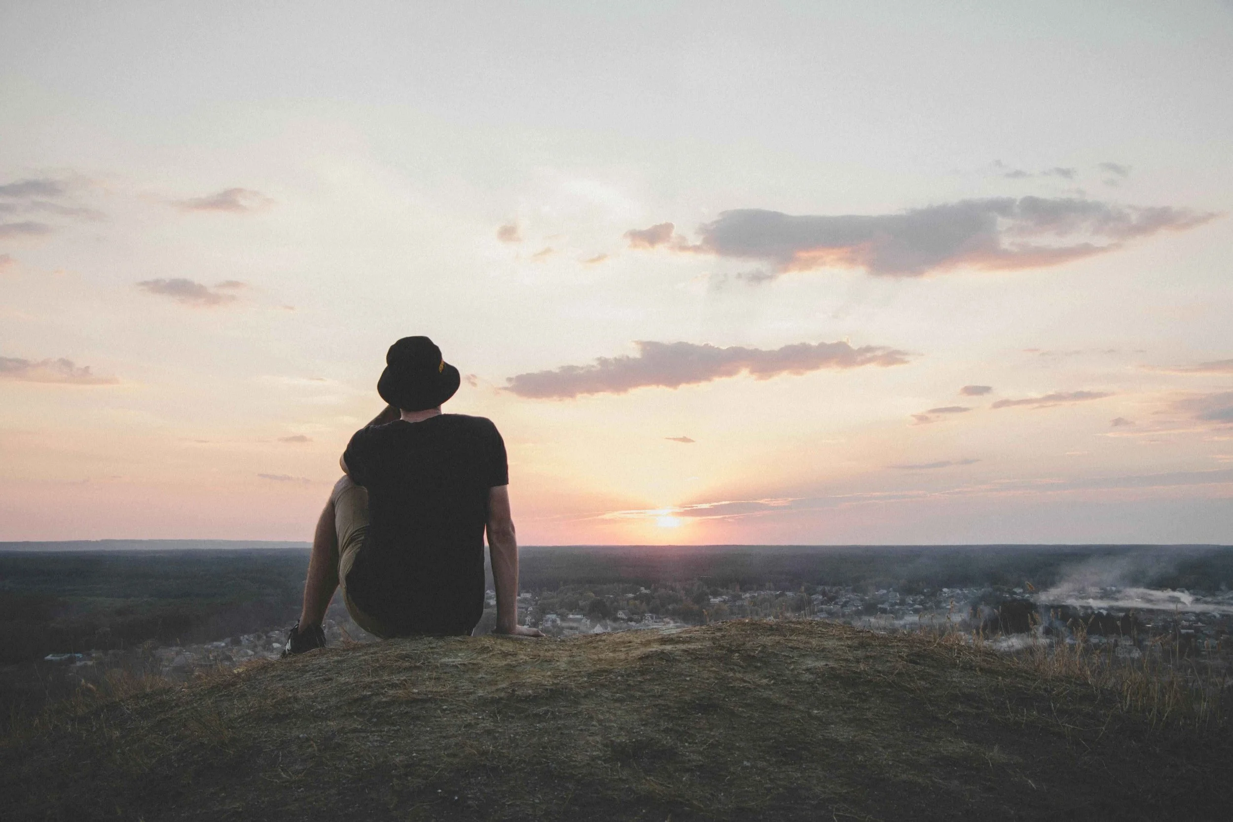 A person seen from behind sitting alone on a hilltop, gazing out toward a vast horizon at sunset — representing the quiet weight of depression and the hope that comes with seeking depression therapy in Los Angeles, CA. 