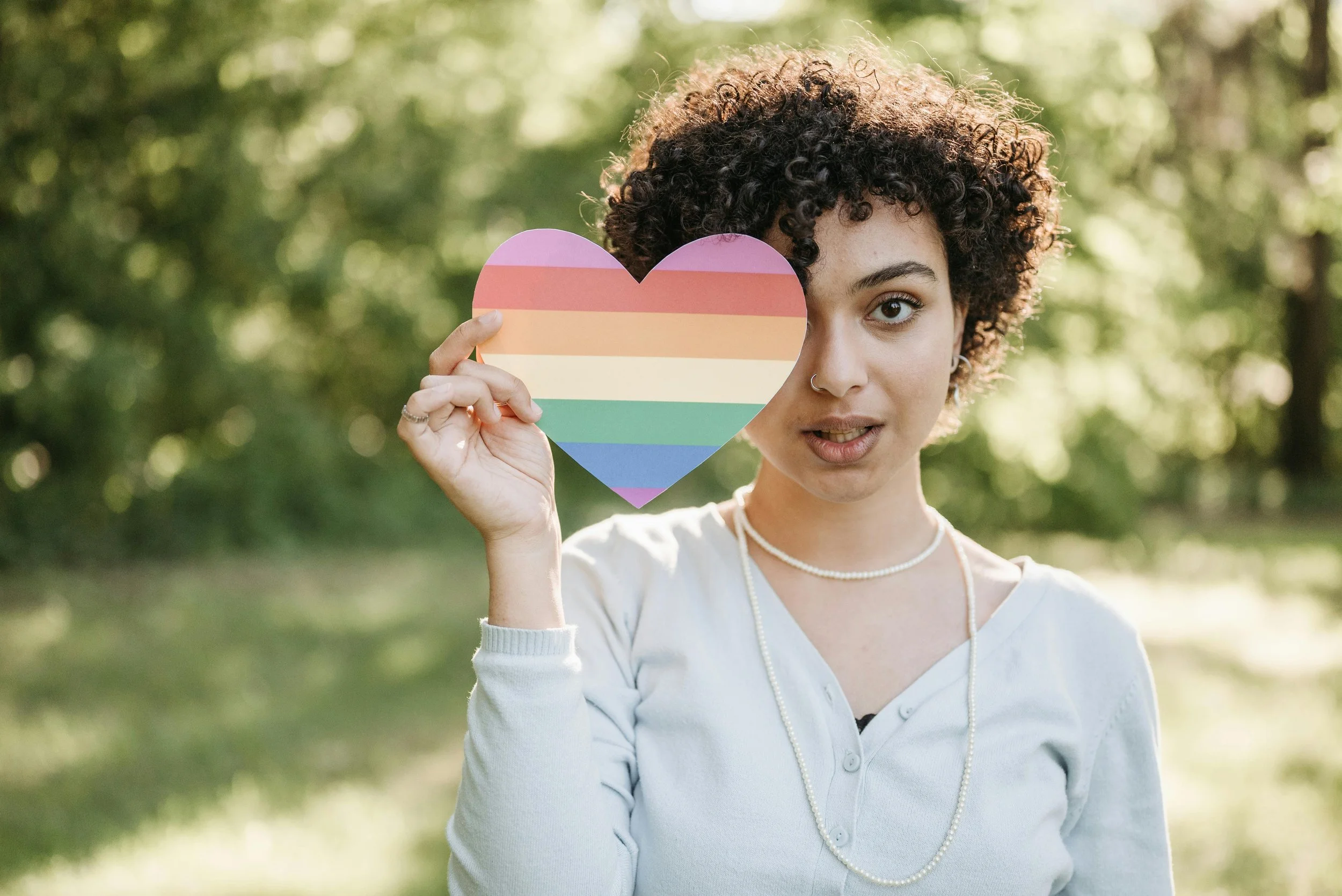 > A young woman outdoors holding a pride rainbow heart, representing affirmation, identity, and safe LGBTQ+ therapy and counseling services in Los Angeles, CA.
